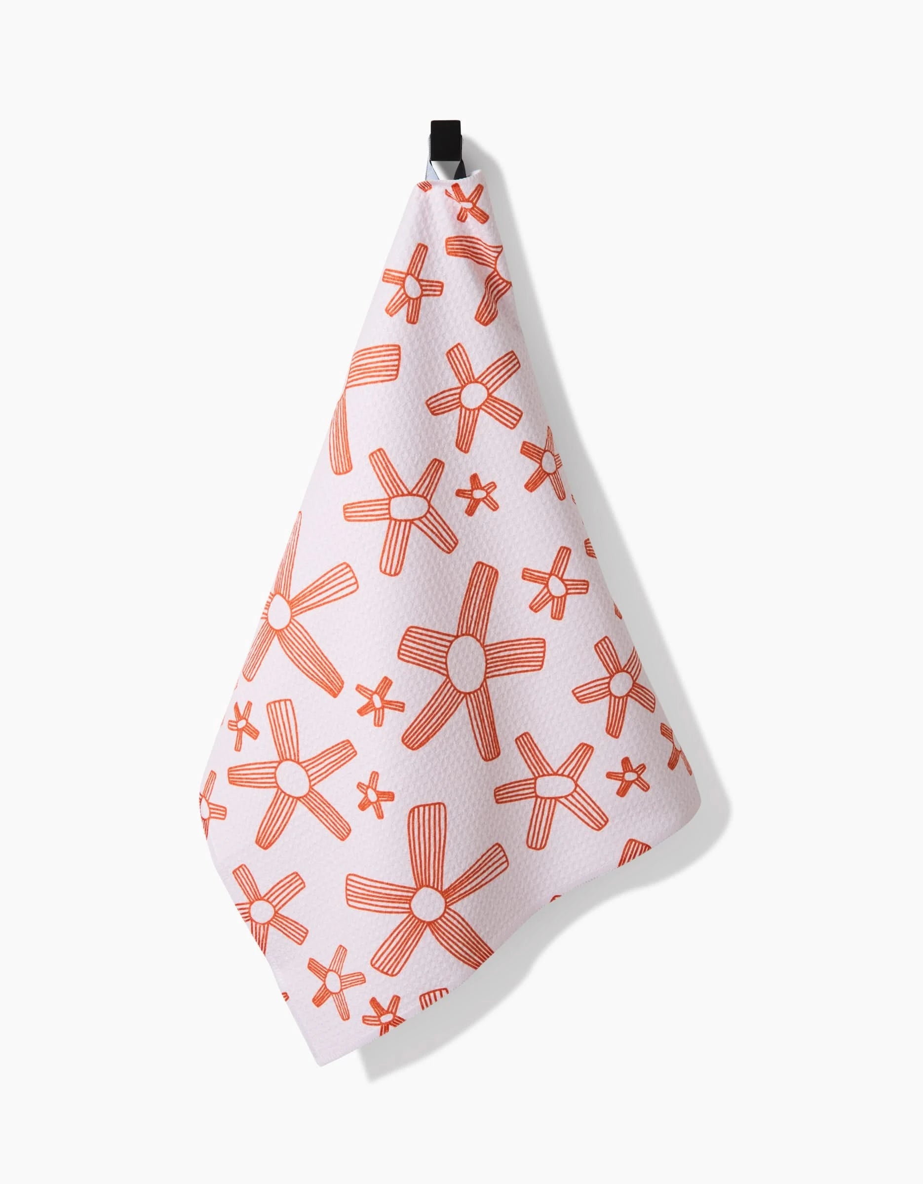 The Chunky Striped Flower tea towel by Coit Creative, crafted from recycled materials, features orange floral patterns with large and small stylized flowers and hangs from a black loop against a plain white background.