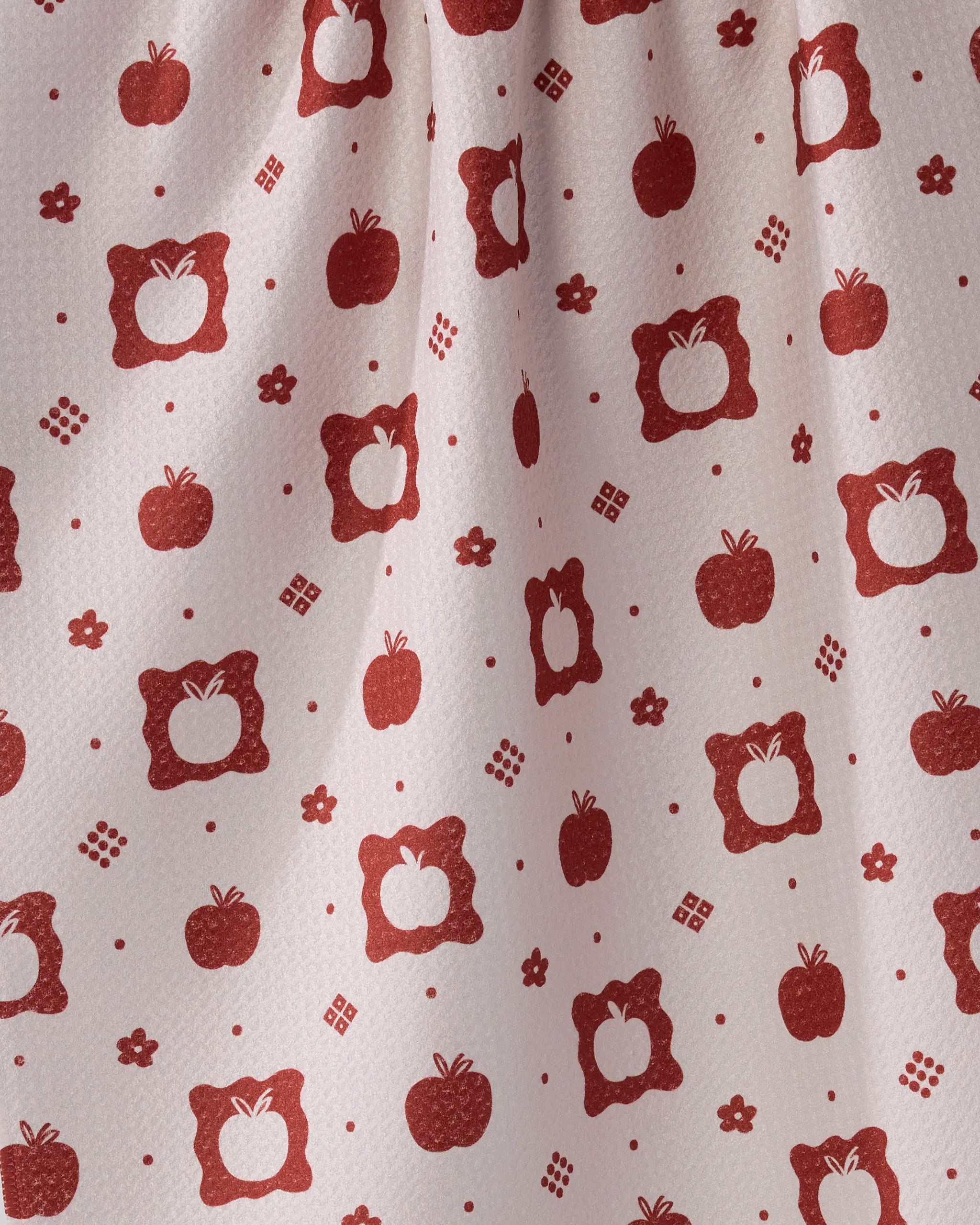 The Geometry Cider Mill tea towel features a pattern of red apples and geometric shapes on light Geoweave fabric. Apples, some plain and some bordered, are evenly spread across the softly textured surface.
