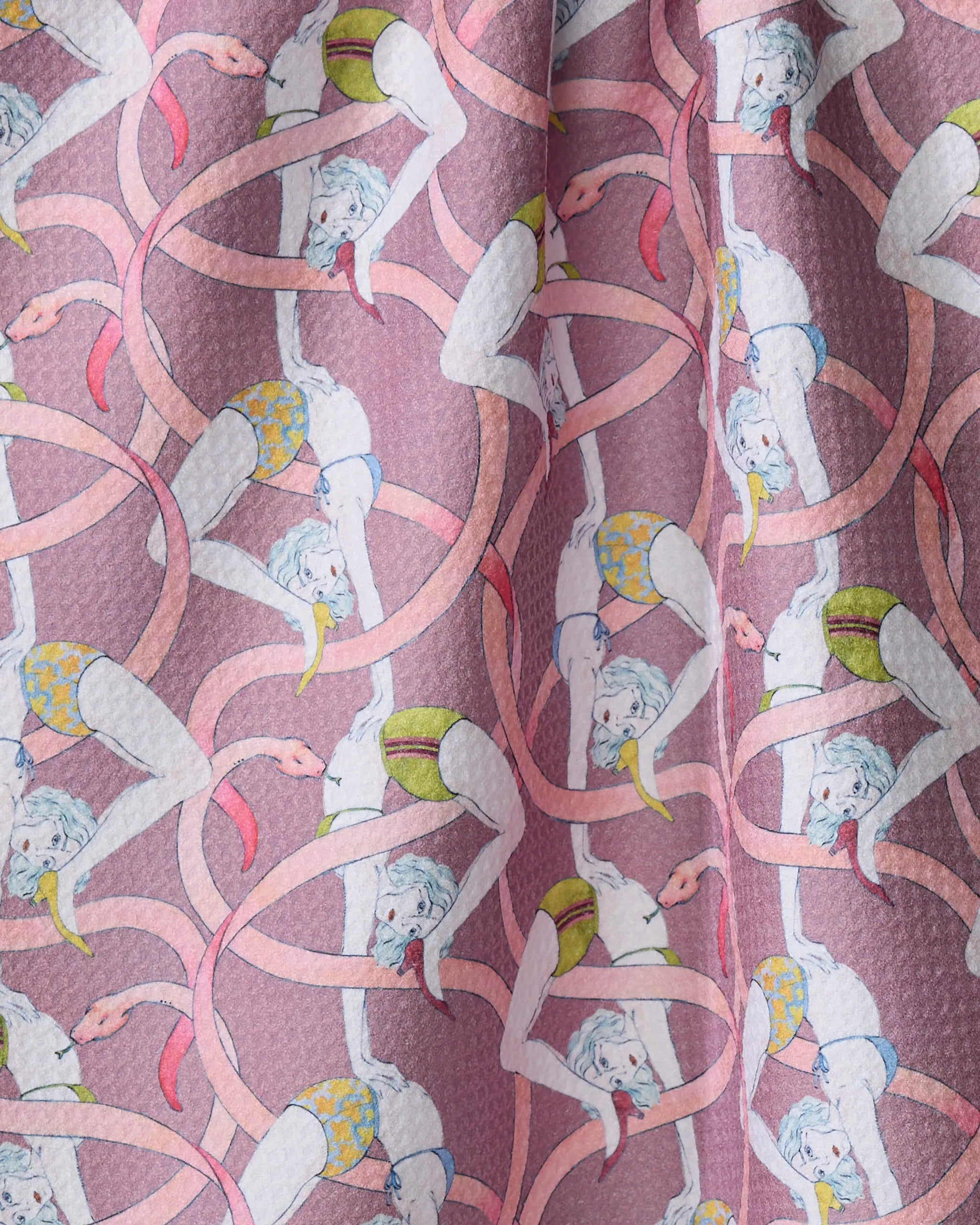 Circus by Maayan Alper-Swan is an eco-friendly, patterned pink kitchen towel featuring playful cartoon figures in yellow shorts doing acrobatic poses with snake-like shapes, all repeating across the textured fabric.