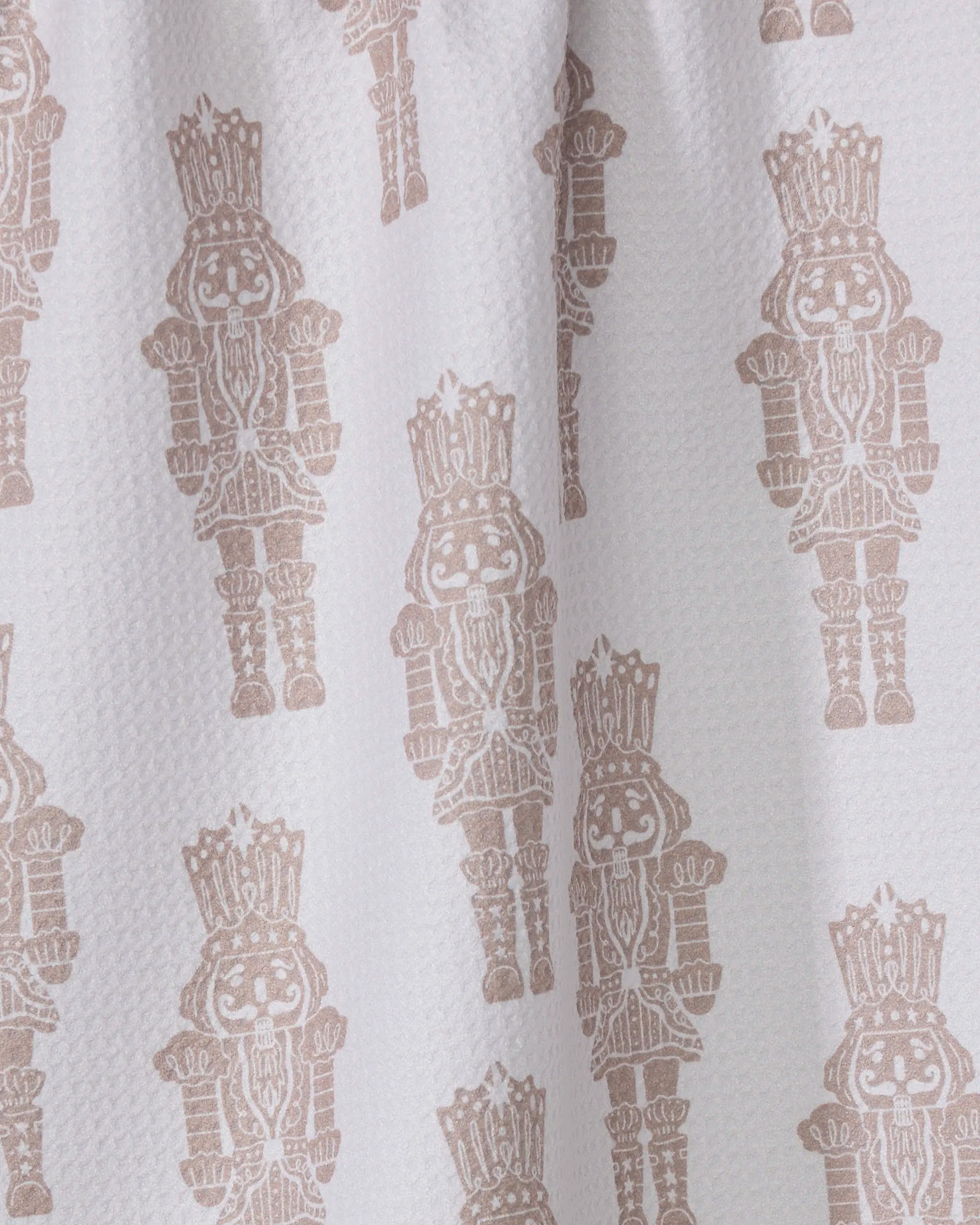 The Geometry Clara dish towel is white and textured, featuring a repeating pattern of light brown nutcracker figures with smiling faces, decorated hats, and detailed uniforms.