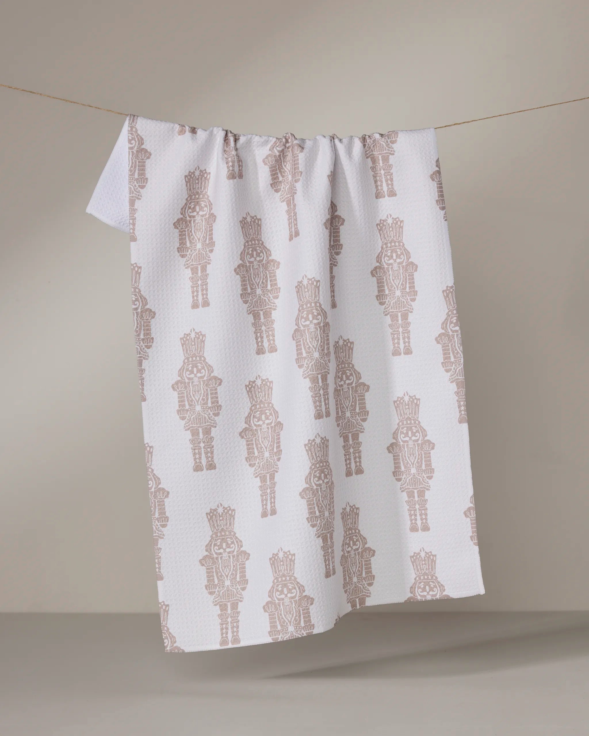 The Geometry Clara tea towel, featuring a brown nutcracker pattern on white, is draped over a clothesline with a plain light gray background.