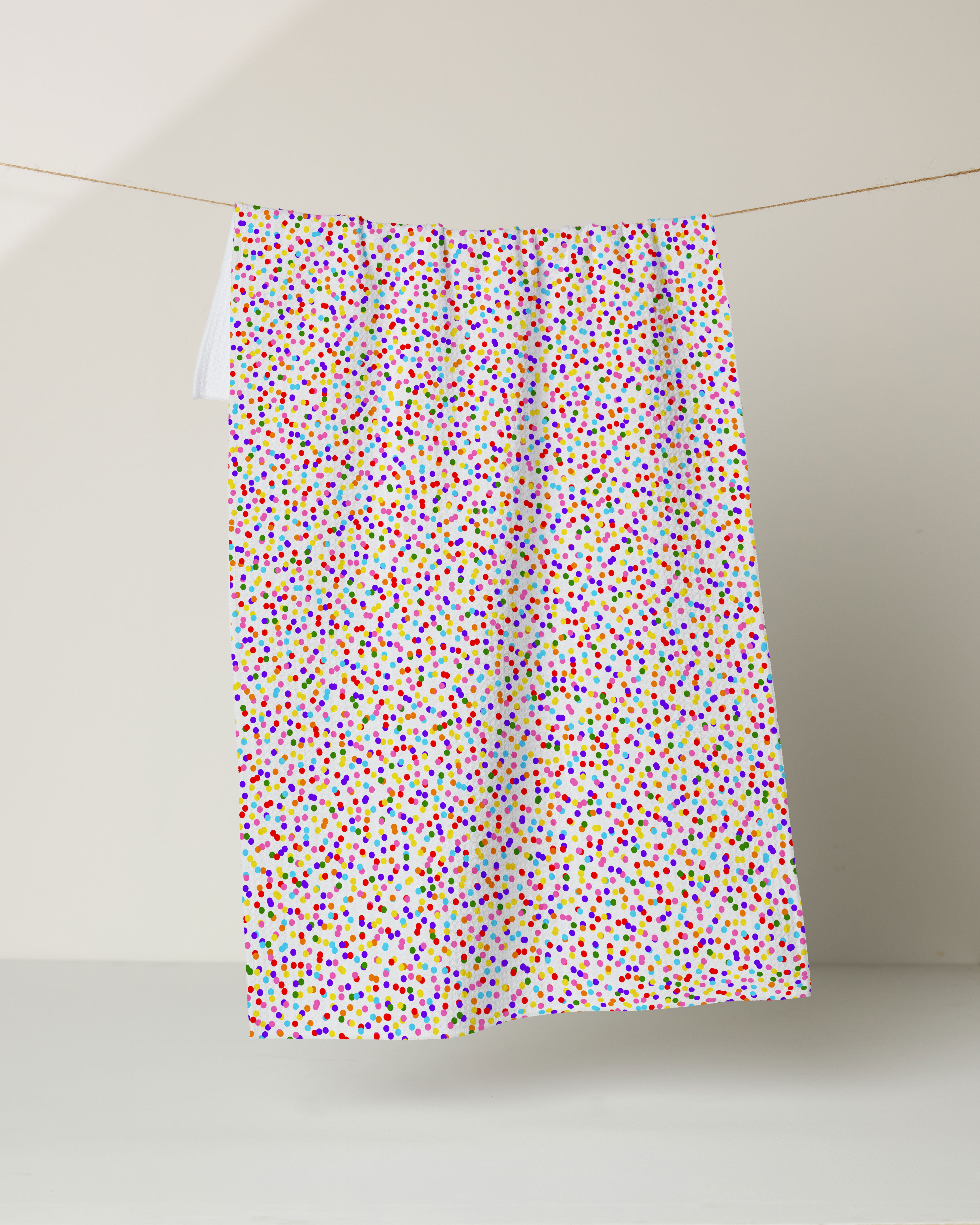 The Geometry Classic Dot Cake recycled kitchen towel, featuring a dense pattern of small, colorful dots, hangs on a clothesline against a plain, light background.