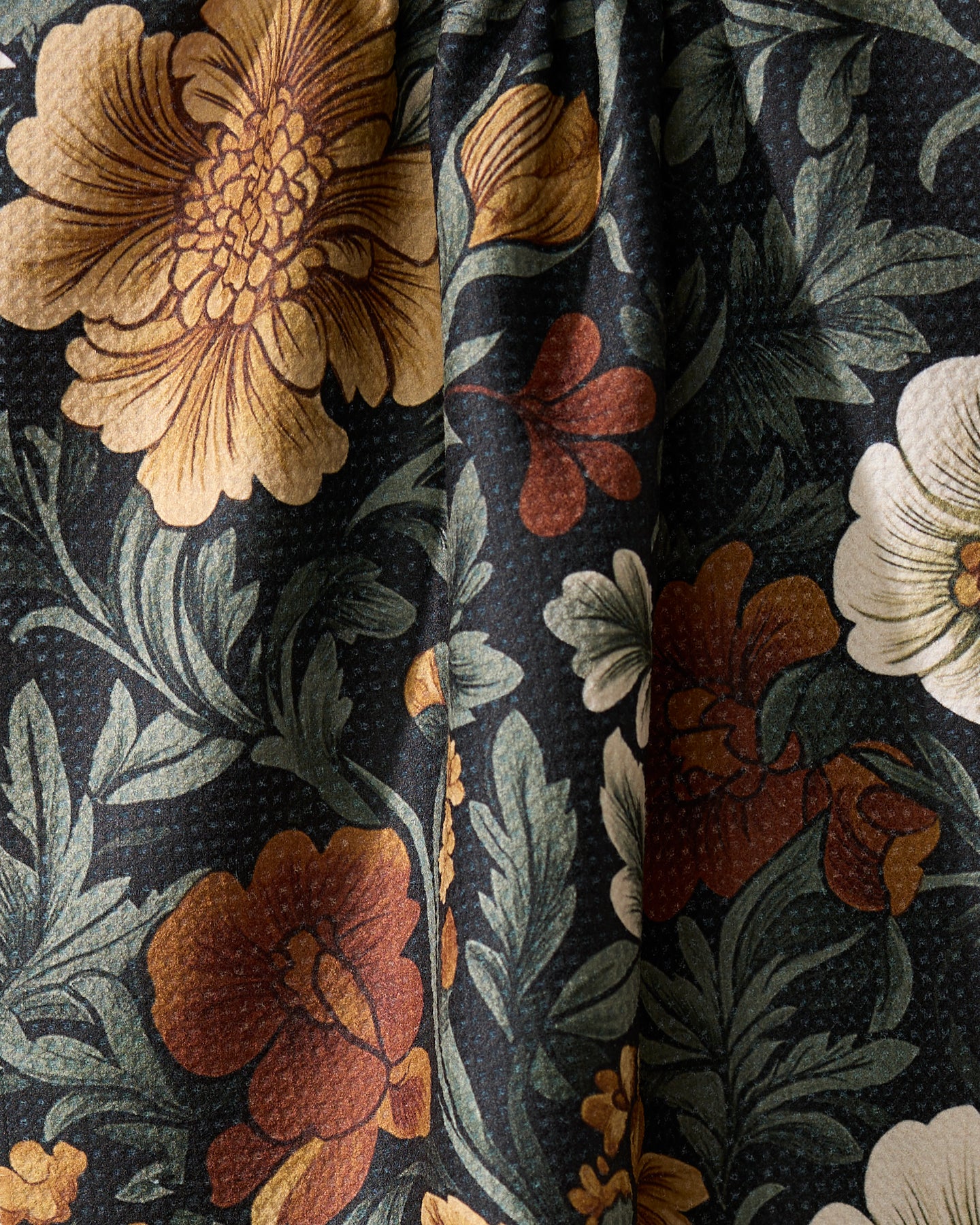 A close-up of Geometry’s Classic Floral kitchen towel, made from recycled materials, draped to show its soft folds and an eco-friendly design with vibrant orange, yellow, and white flowers on a dark background.