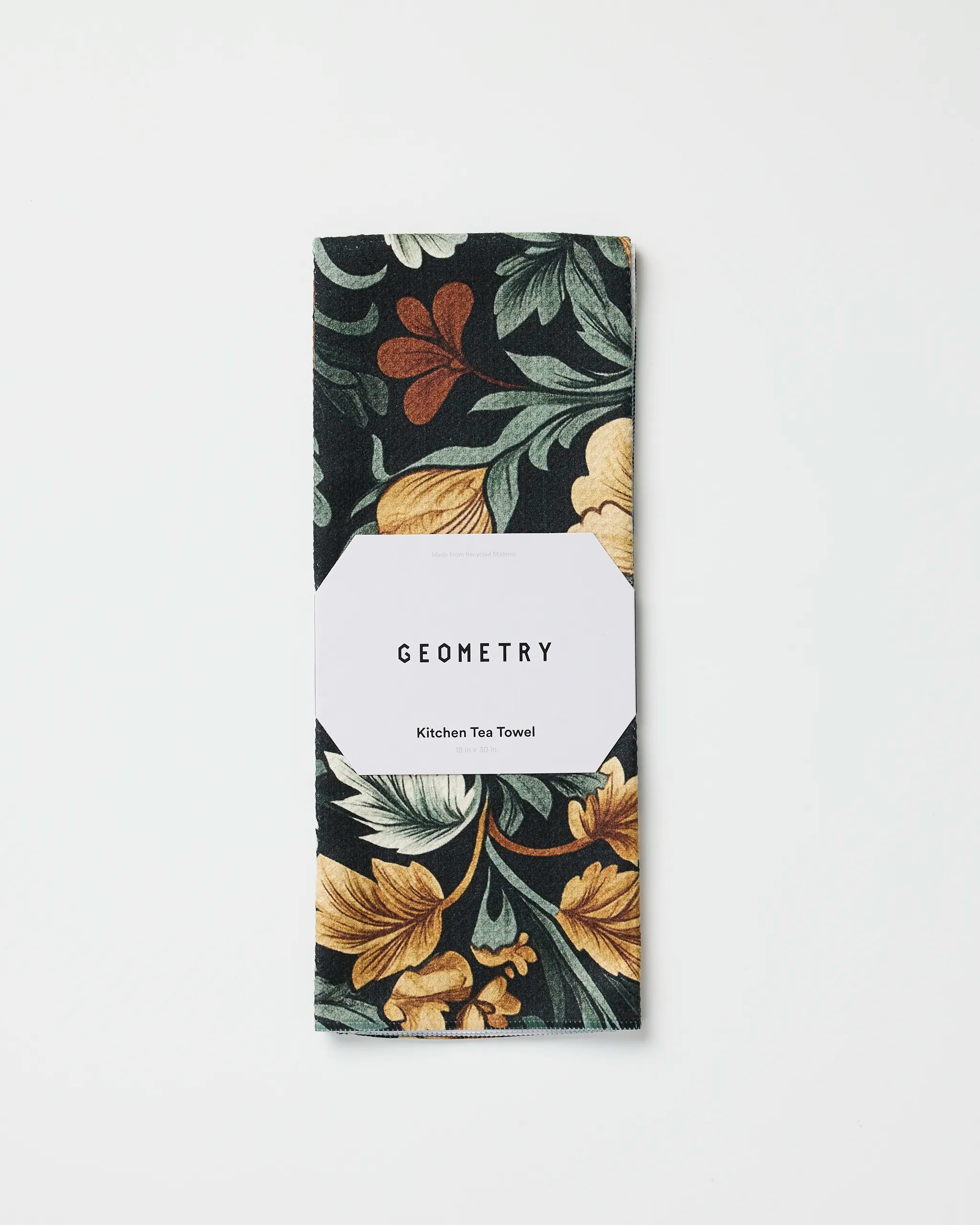 A folded eco-friendly Geometry Kitchen Tea Towel in the Classic Floral dark print with yellow, green, and rust accents, wrapped in a white label displaying the brand name. Set against a white background.