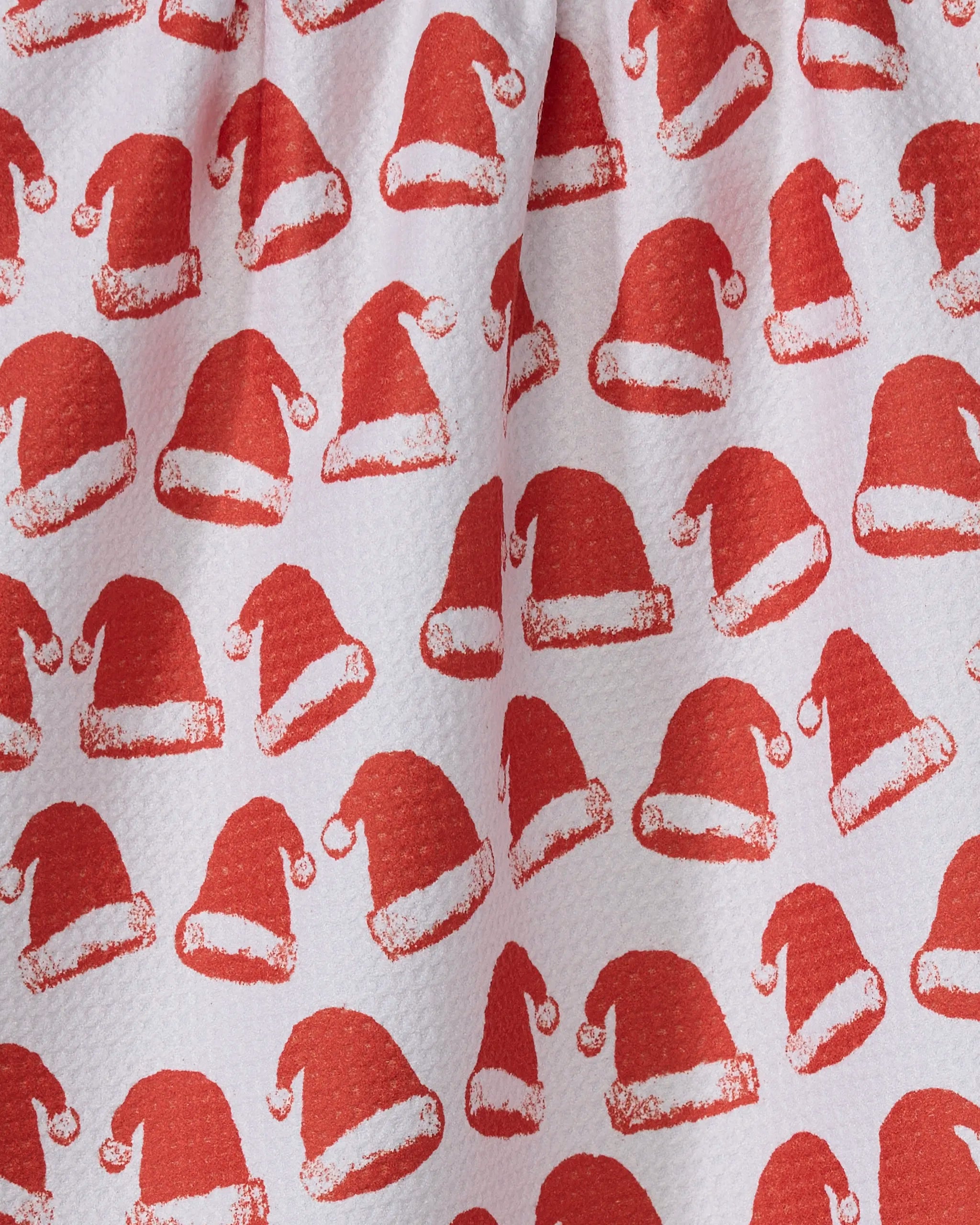 Close-up of Geometry’s Clausen tea towel, crafted from recycled materials with rows of red Santa hats and fluffy white trim. The ultra-absorbent fabric features soft wrinkles and subtle shadows.