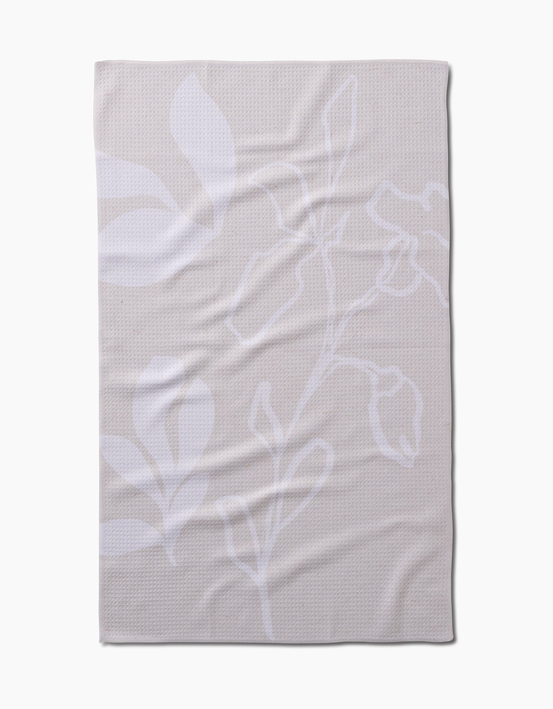 The GEOMETRY Clean blanket is beige with a subtle white floral pattern of large leaves and flower outlines, crafted from recycled materials. It is shown laid flat with gentle wrinkles visible.