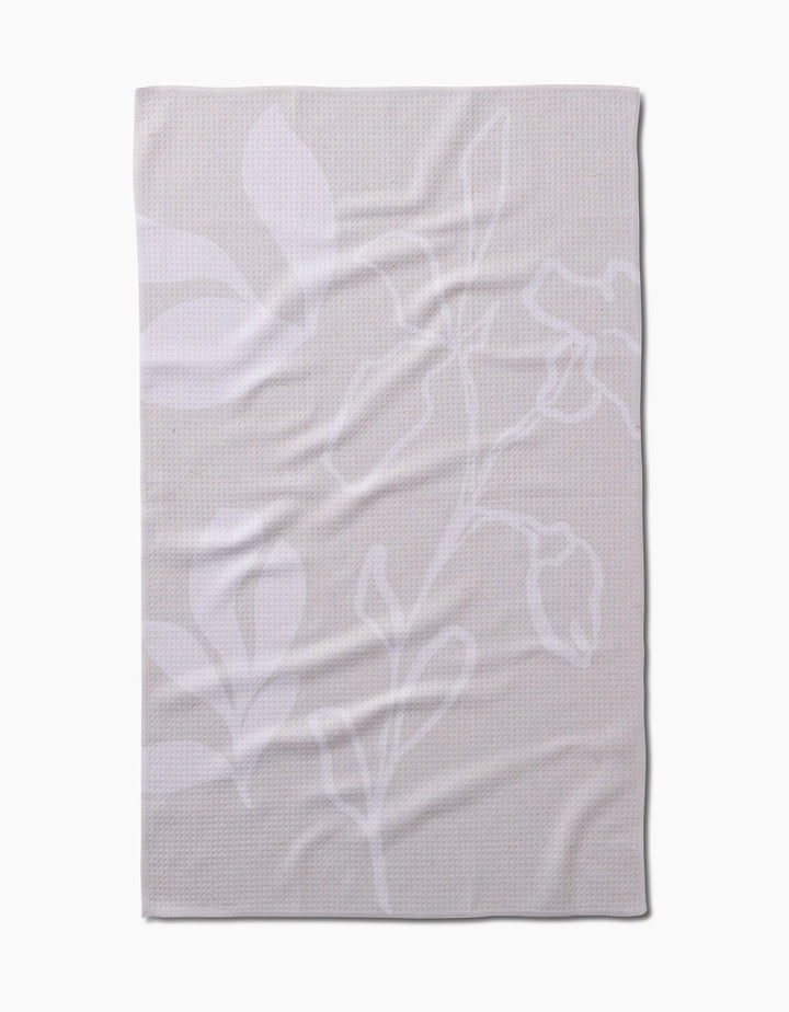 The GEOMETRY Clean blanket is beige with a subtle white floral pattern of large leaves and flower outlines, crafted from recycled materials. It is shown laid flat with gentle wrinkles visible.