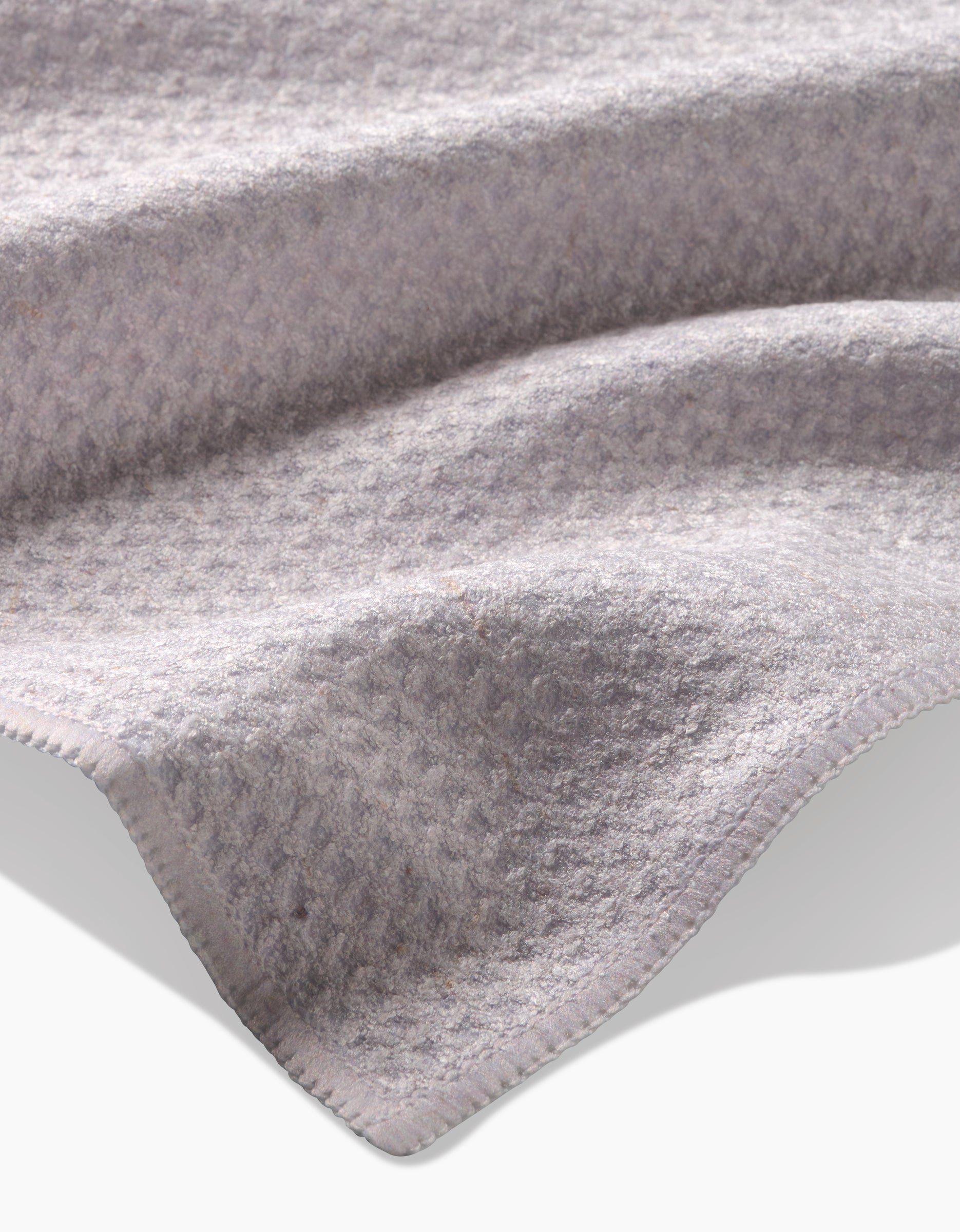 A close-up of Clean by GEOMETRY: a soft, light gray Geoweave tea towel with subtle raised patterns, curved folds, stitched edges, and an eco-friendly blend of recycled materials.