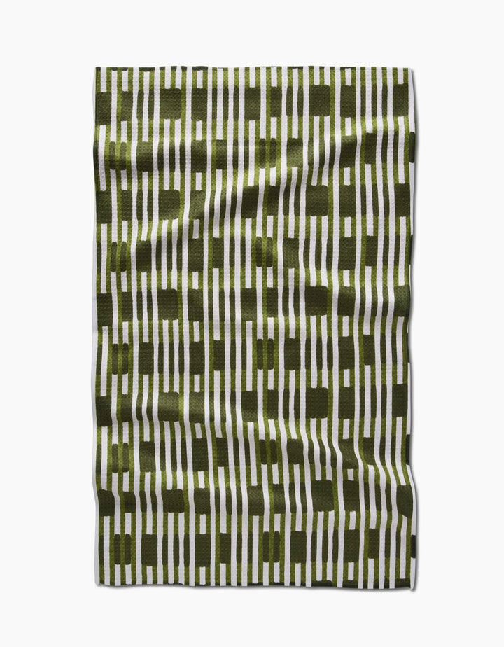 The GEOMETRY Clover Stripe tea towel features vertical olive green and white stripes with intersecting olive green blocks, shown laid flat on a white background with a slightly wrinkled fabric texture.