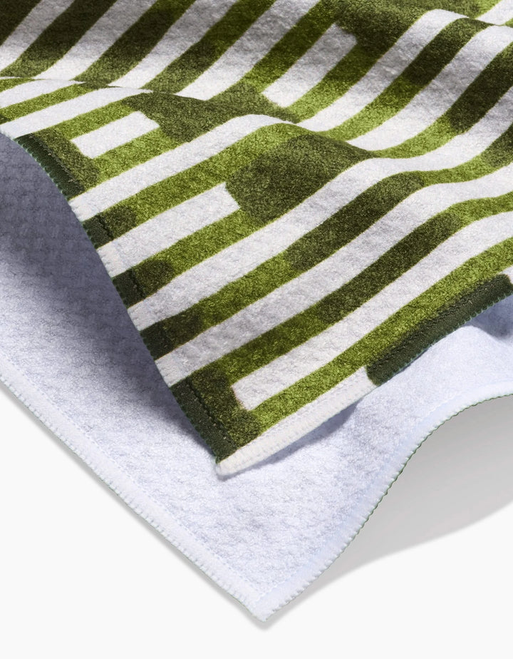 A close-up of the GEOMETRY Clover Stripe dish towel, featuring a green and white geometric stripe design on the soft front and a plain white textured back.