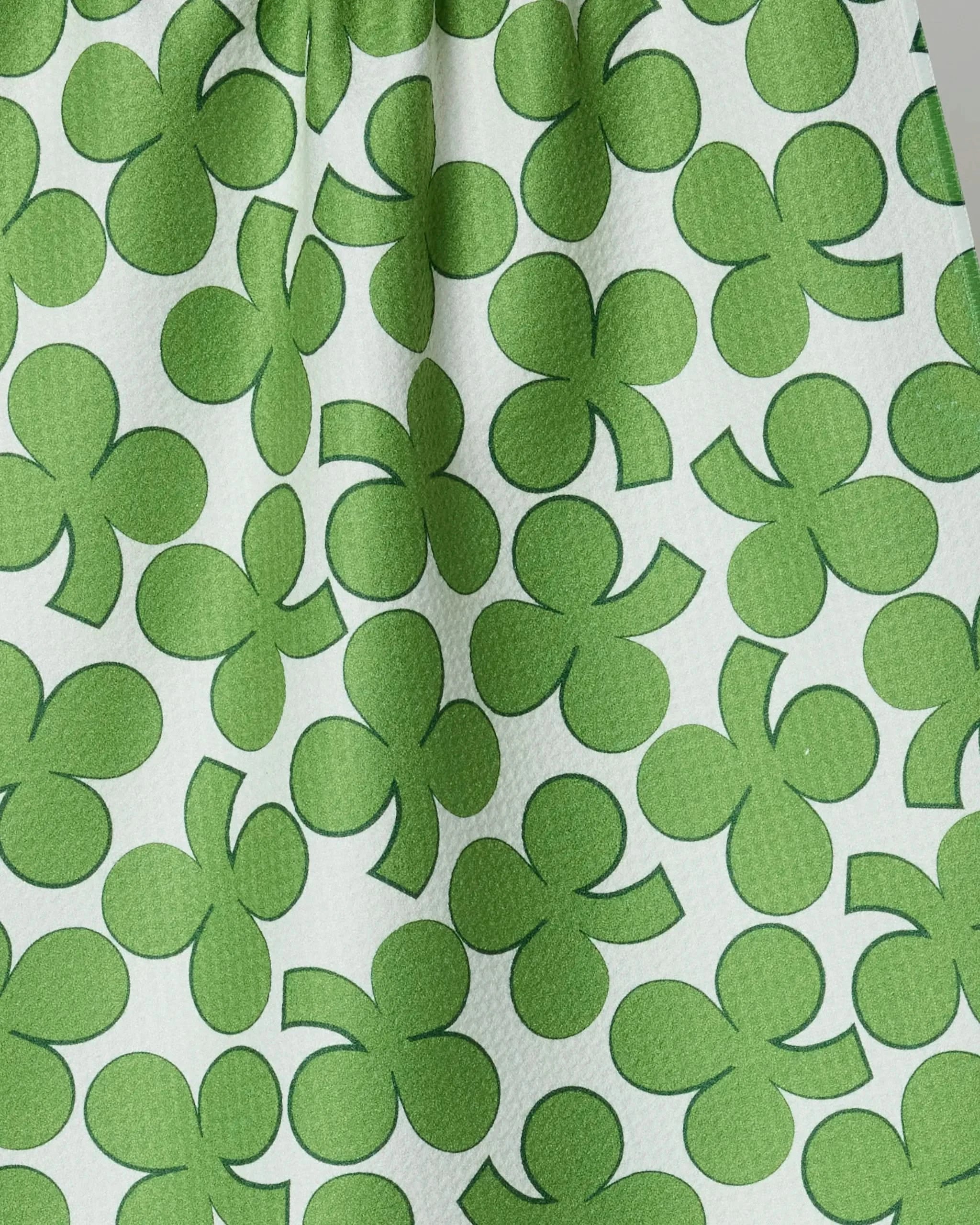 Close-up of the Geometry Clover Toss dish towel, showing its absorbent, textured fabric and repeating green shamrocks on a white background—stylish and practical for any kitchen.