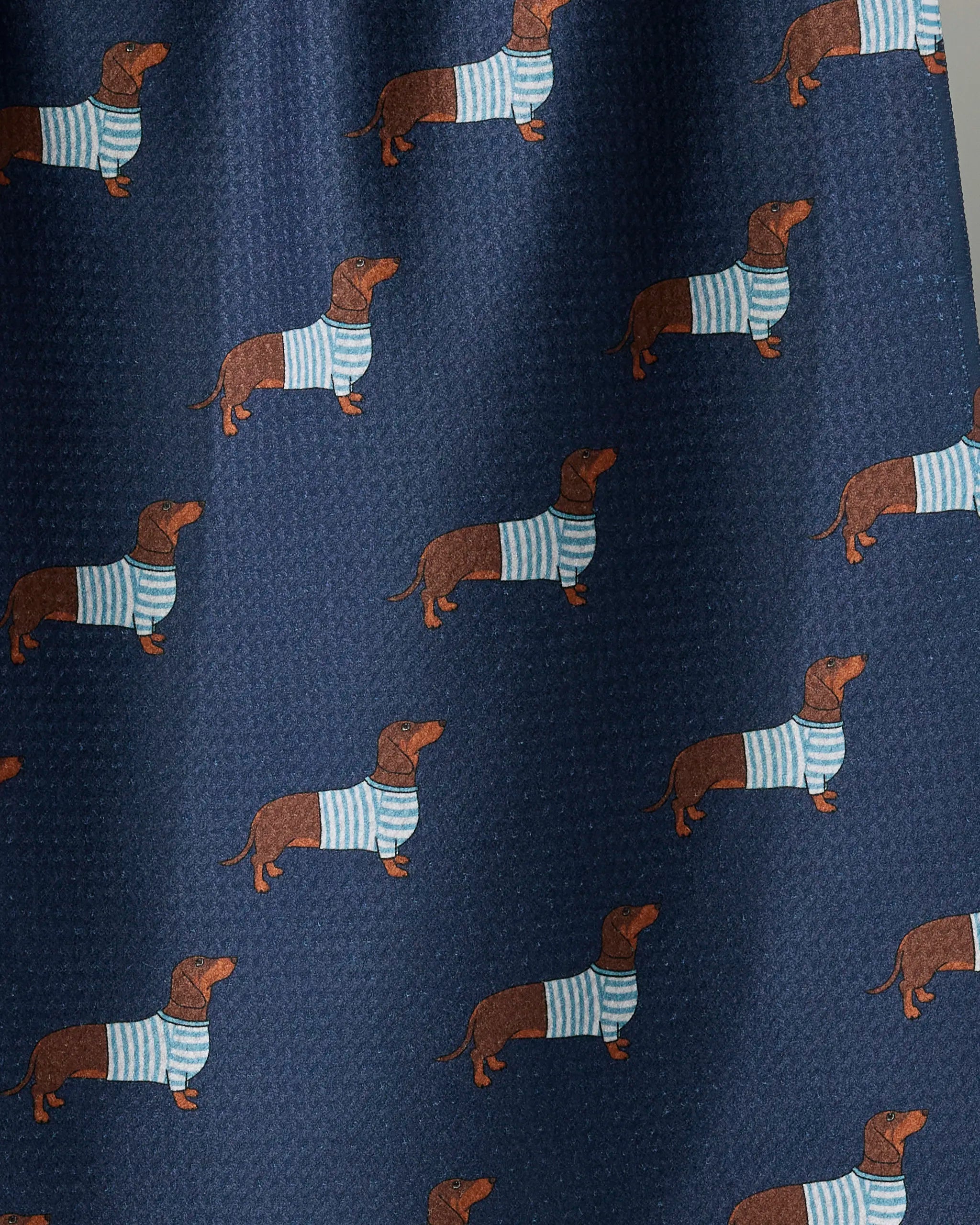 Introducing the “Coastal Dachshund” kitchen towel by Geometry, featuring a navy blue background adorned with a repeating pattern of brown dachshunds in light blue and white striped sweaters, thoughtfully crafted from recycled materials.