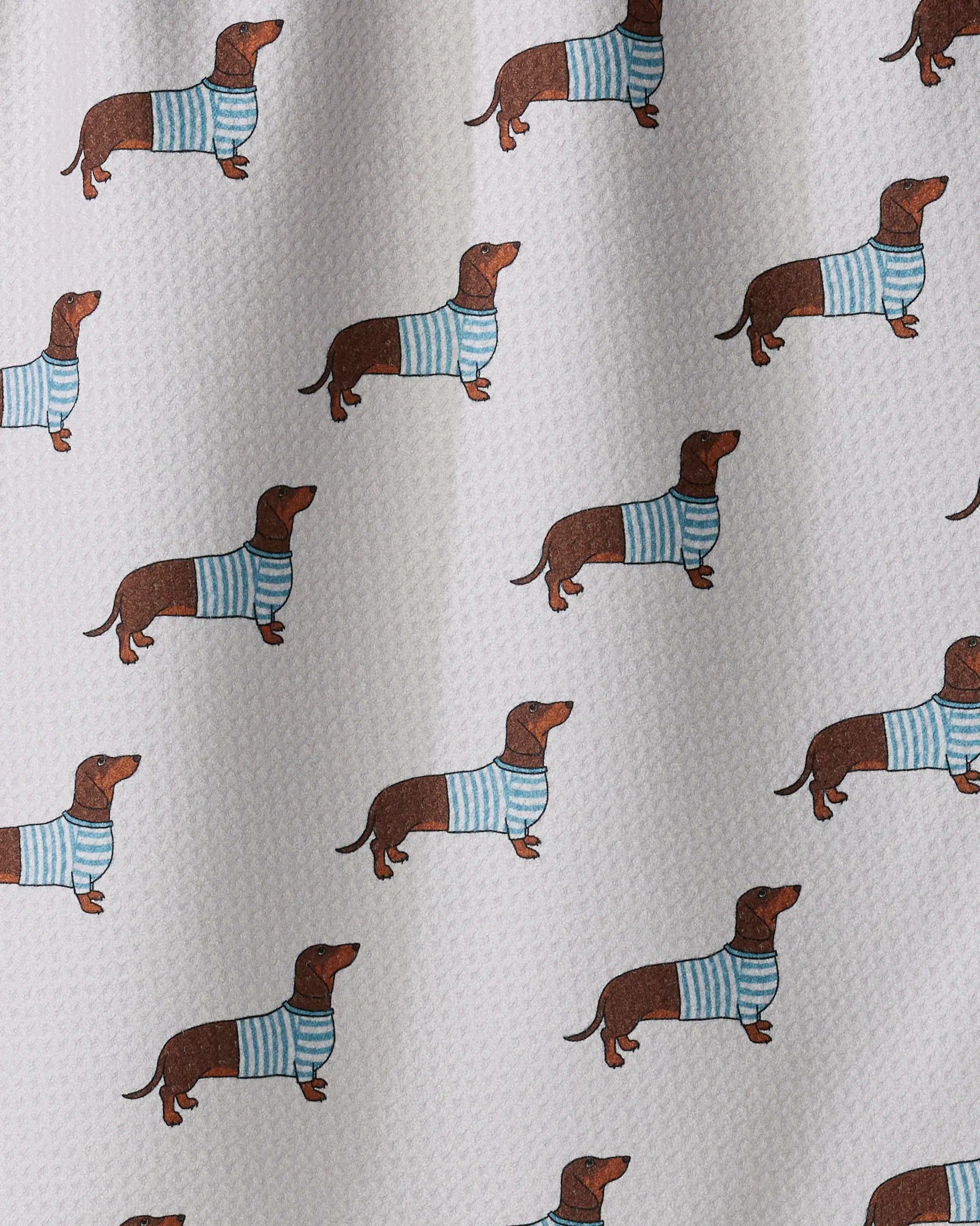 Introducing the “Coastal Dachshund” tea towel by Geometry, featuring a playful pattern of dachshunds sporting blue and white striped sweaters on a white textured background. The evenly spaced dogs facing various directions create an engaging design, perfect for adding charm to any kitchen. Made from recycled materials.
