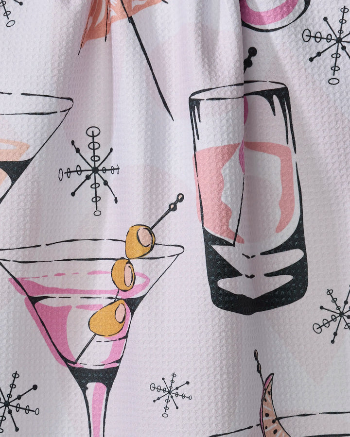 A close-up of Julianne Haness's "Cocktail Hour" tea towel, ultra-absorbent and made from recycled materials, features a retro print with martini glasses, pink drinks, and atomic starbursts on a white textured background.