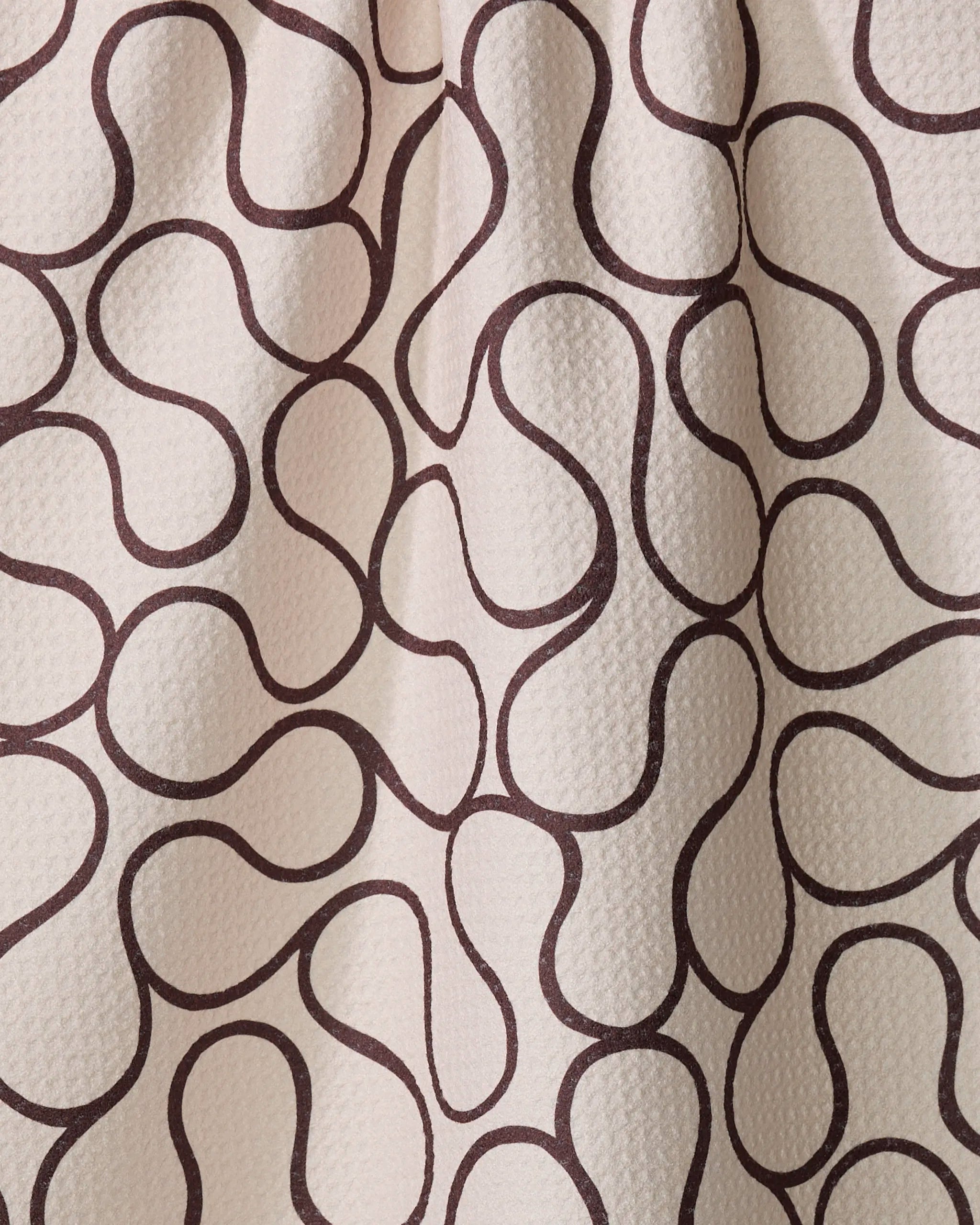A close-up of Gerdadzy's Coffee Swirl shows cream-colored textured fabric with an abstract pattern of wavy, interconnected brown lines.