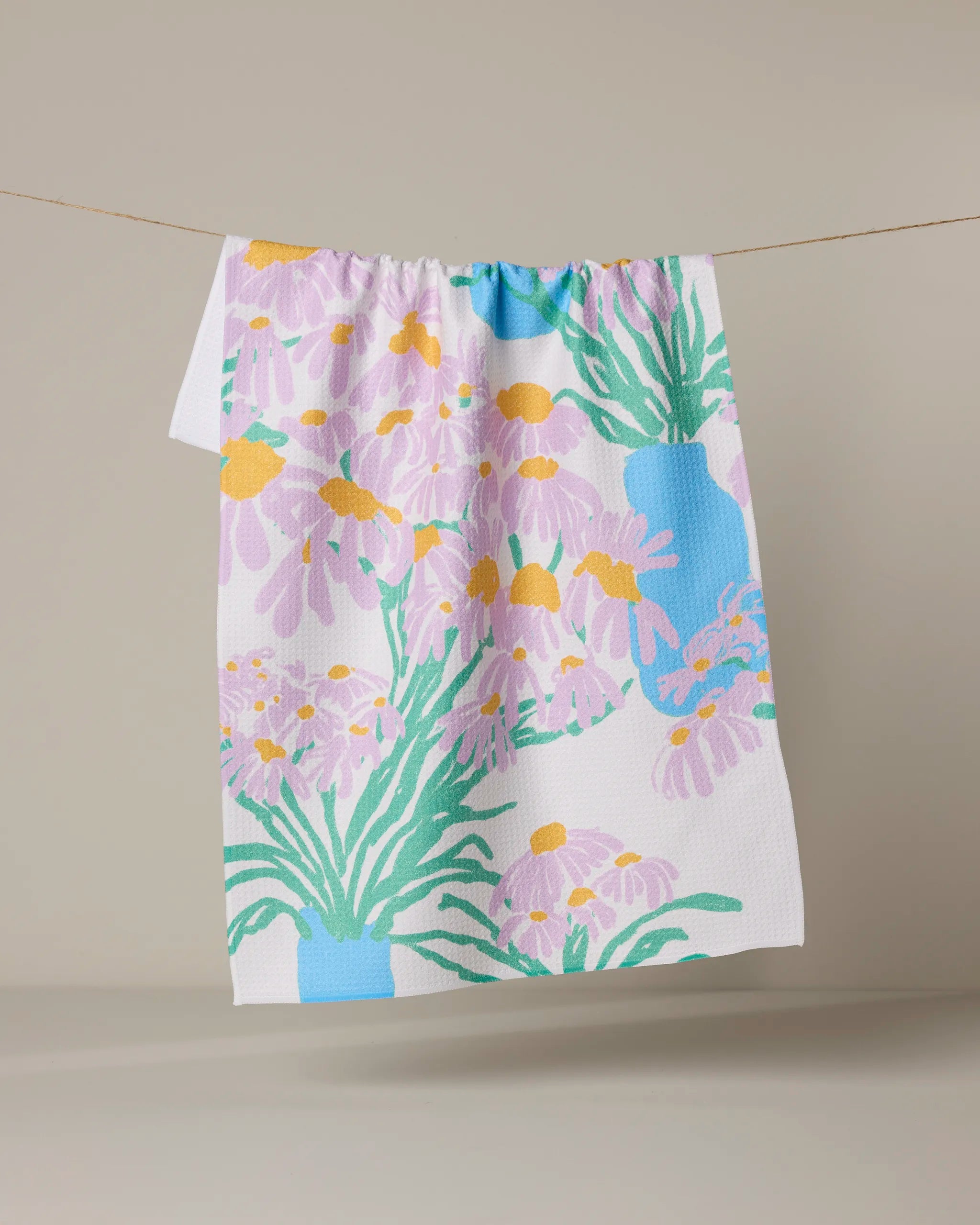 The Geometry Colette tea towel features a colorful floral design with purple flowers, yellow centers, green leaves, and blue vases. Eco-friendly and bright, it adds a cheerful touch to your kitchen decor.