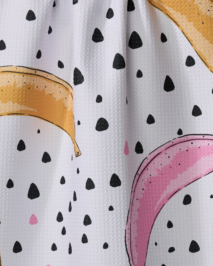 The Color Pop Bananas tea towel by Julianne Haness features a playful yellow and pink banana pattern with black dots on white, crafted from recycled materials.