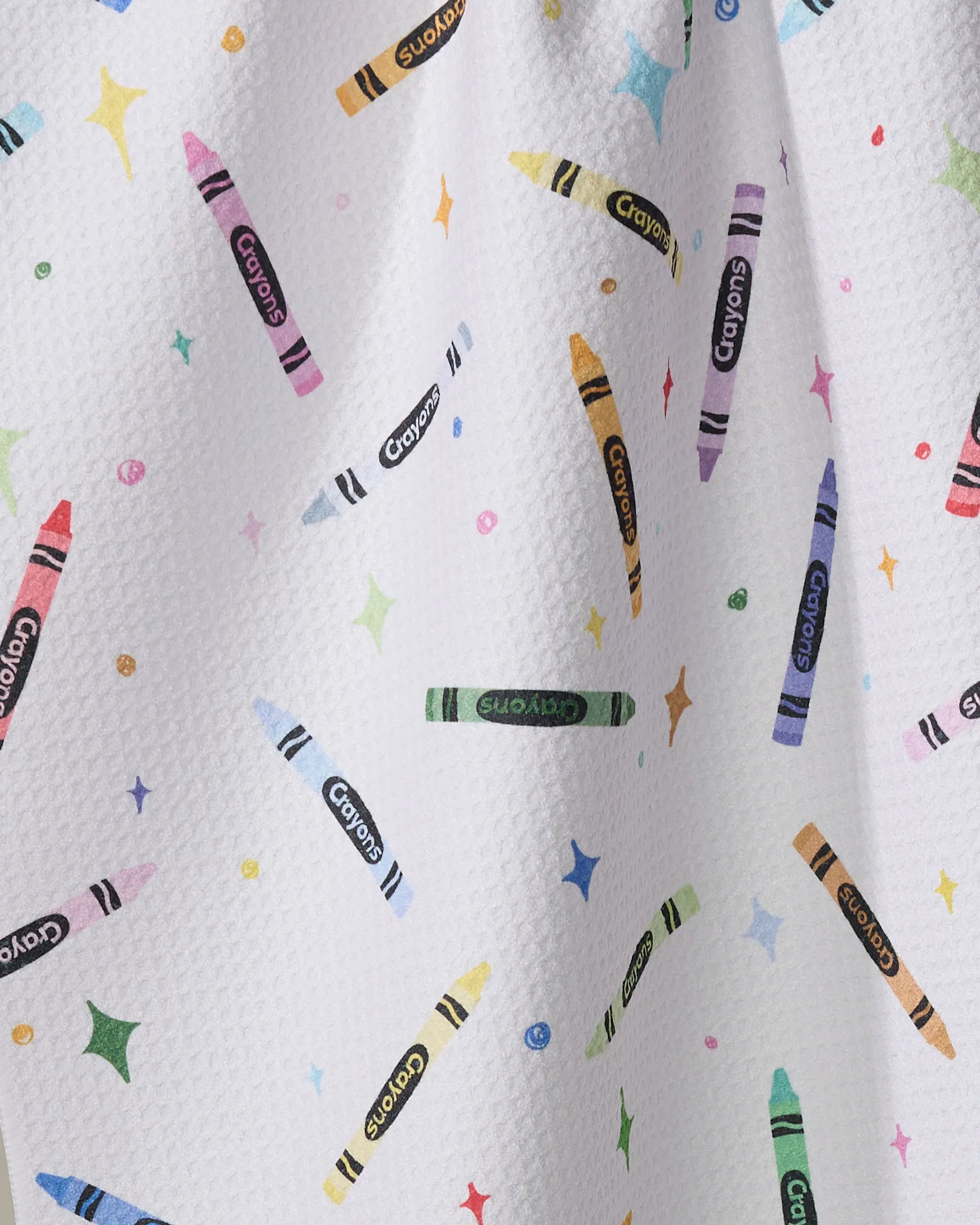 The "Colored Crayons" tea towel by Vaishali Design Studio has a white textured surface decorated with vibrant crayon illustrations and playful stars, made from quick-drying fabric for a fun and practical addition to your kitchen.