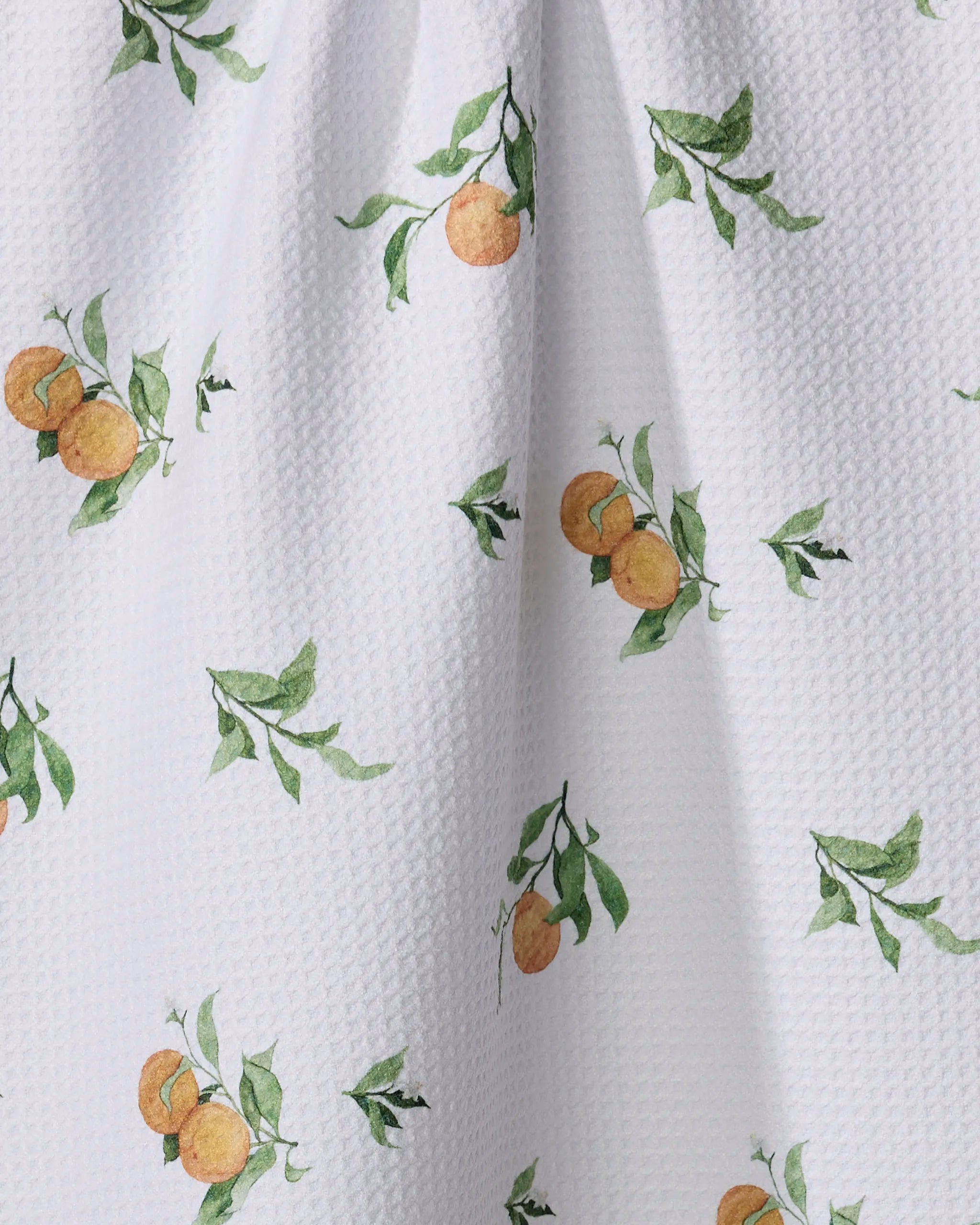 The Aubrey Fairchild Comfort Fruit recycled kitchen towel features white textured fabric with a watercolor orange and green leaf pattern, adding eco-friendly charm and style to your space.