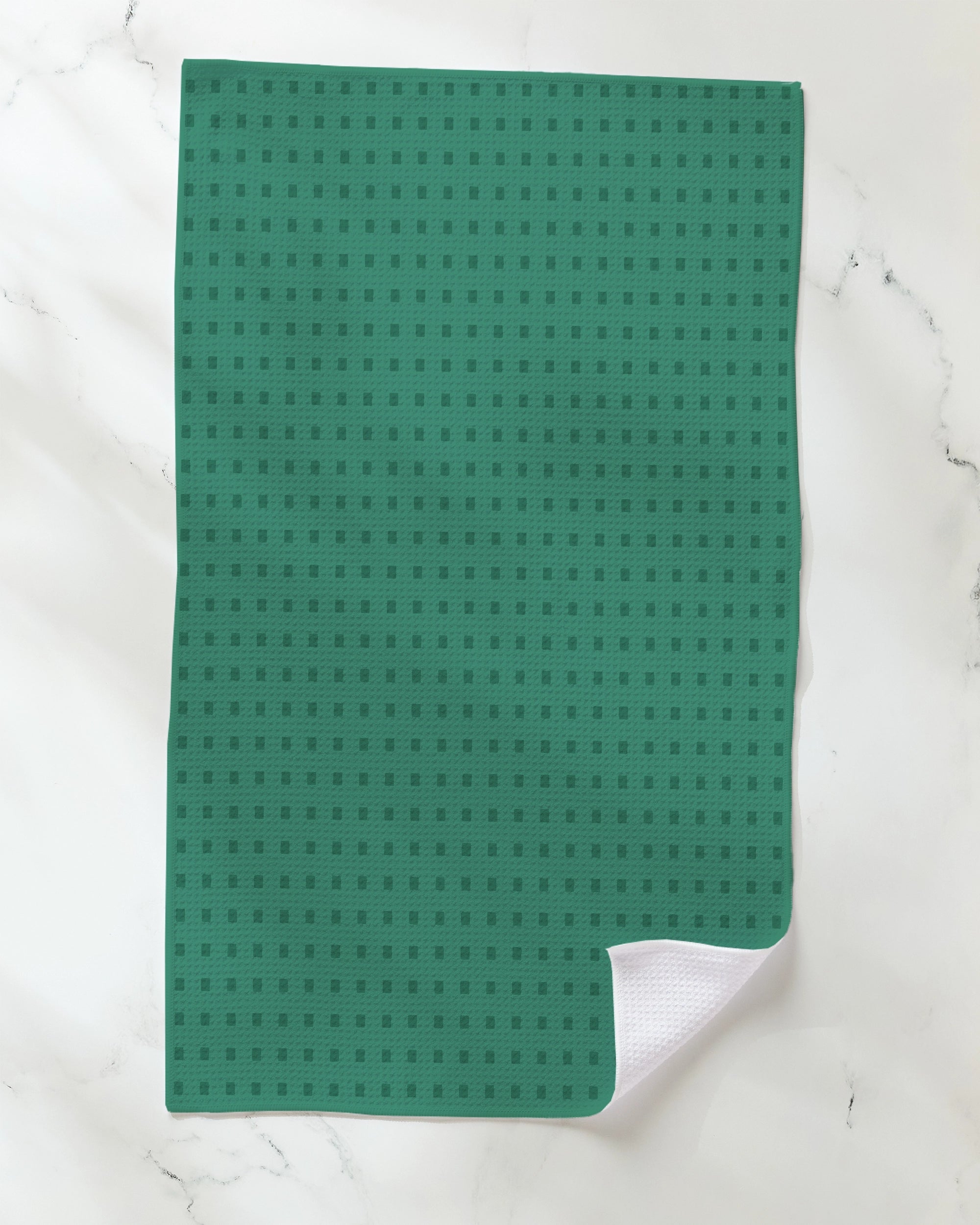 A Confetti Tiles tea towel by Geometry, featuring a playful checkered pattern, rests on a white marble surface with one corner gently folded to show the white underside.