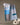 The Geometry “Cool Blocks” recycled kitchen towel, featuring a blue, gray, and white pattern, hangs on a string against a neutral background with two modern abstract white vases positioned to its right.