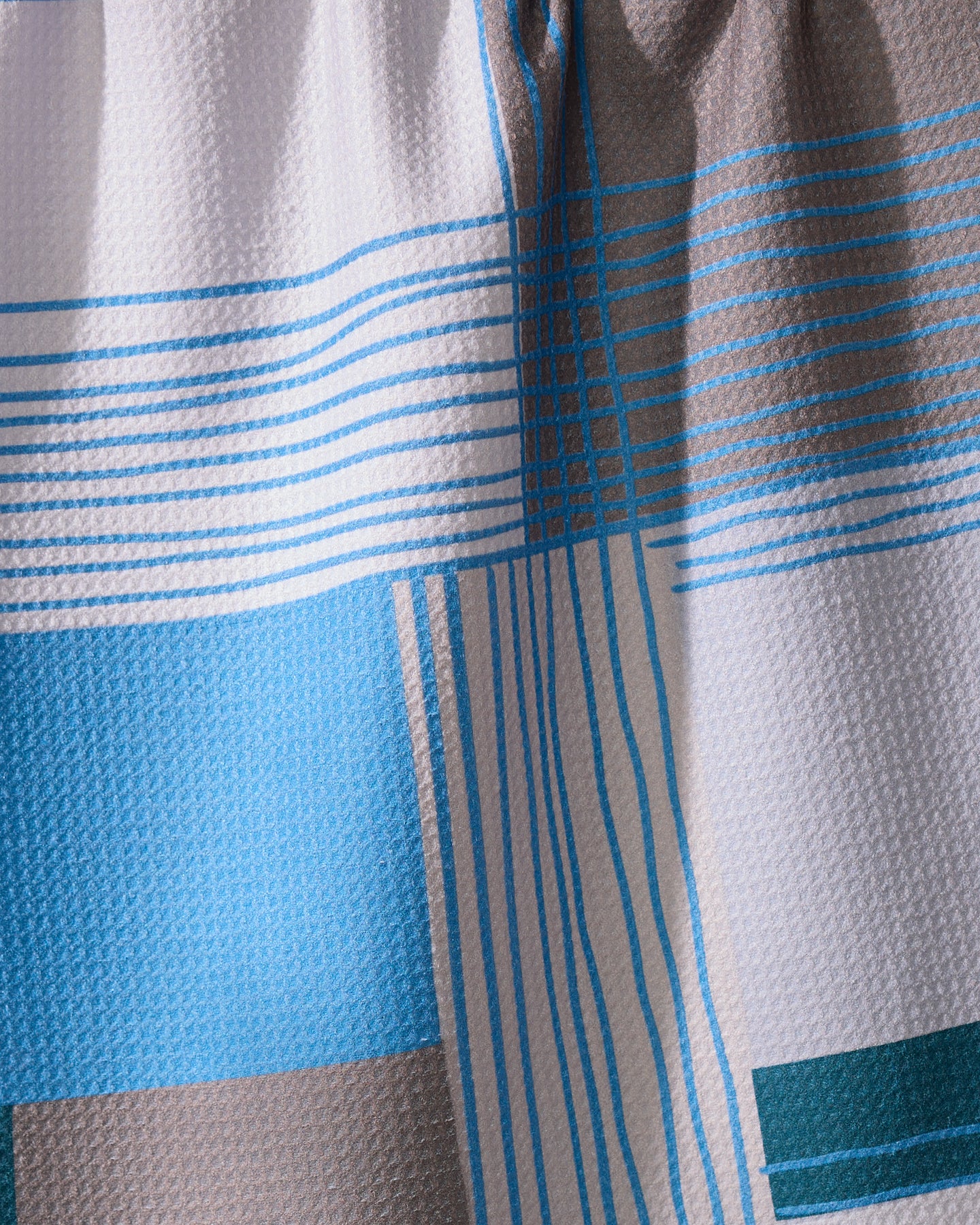 A close-up of Geometrys Cool Blocks towel, showcasing a quick-drying fabric with a geometric blue, gray, and white block pattern accented by intersecting blue lines. The material is slightly gathered at the top.