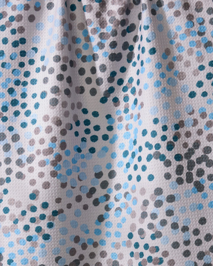 A close-up of Geometry’s Cool Dots kitchen towel shows its textured, ultra-absorbent recycled fabric with an abstract pattern of blue, gray, and black dots scattered on white, highlighted by gentle folds and shadows.