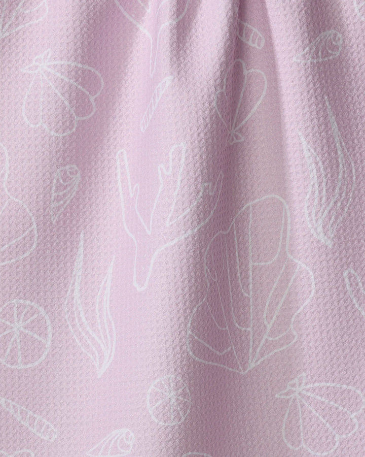 Coral Cove by Janna Sue Design is a light pink recycled kitchen towel featuring white line drawings of shells, seaweed, coral, and citrus slices for a subtle nautical look.