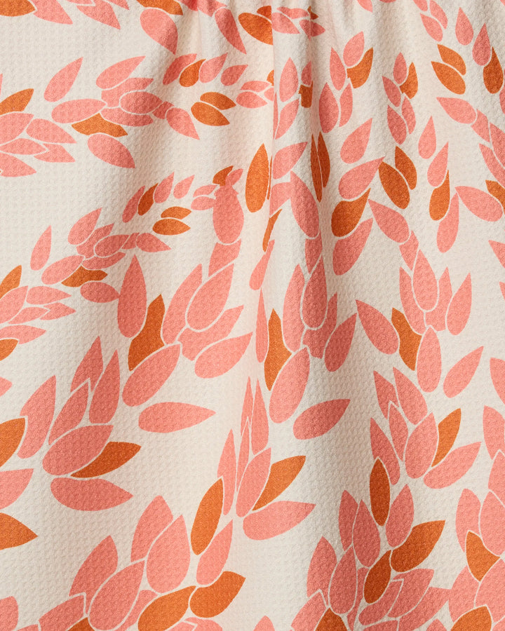Close-up of Geometry’s Coral Drift tea towel, featuring a textured, ultra-absorbent fabric made from recycled materials and a repeating pink and orange leaf-pattern on off-white; the top of the towel is slightly gathered.