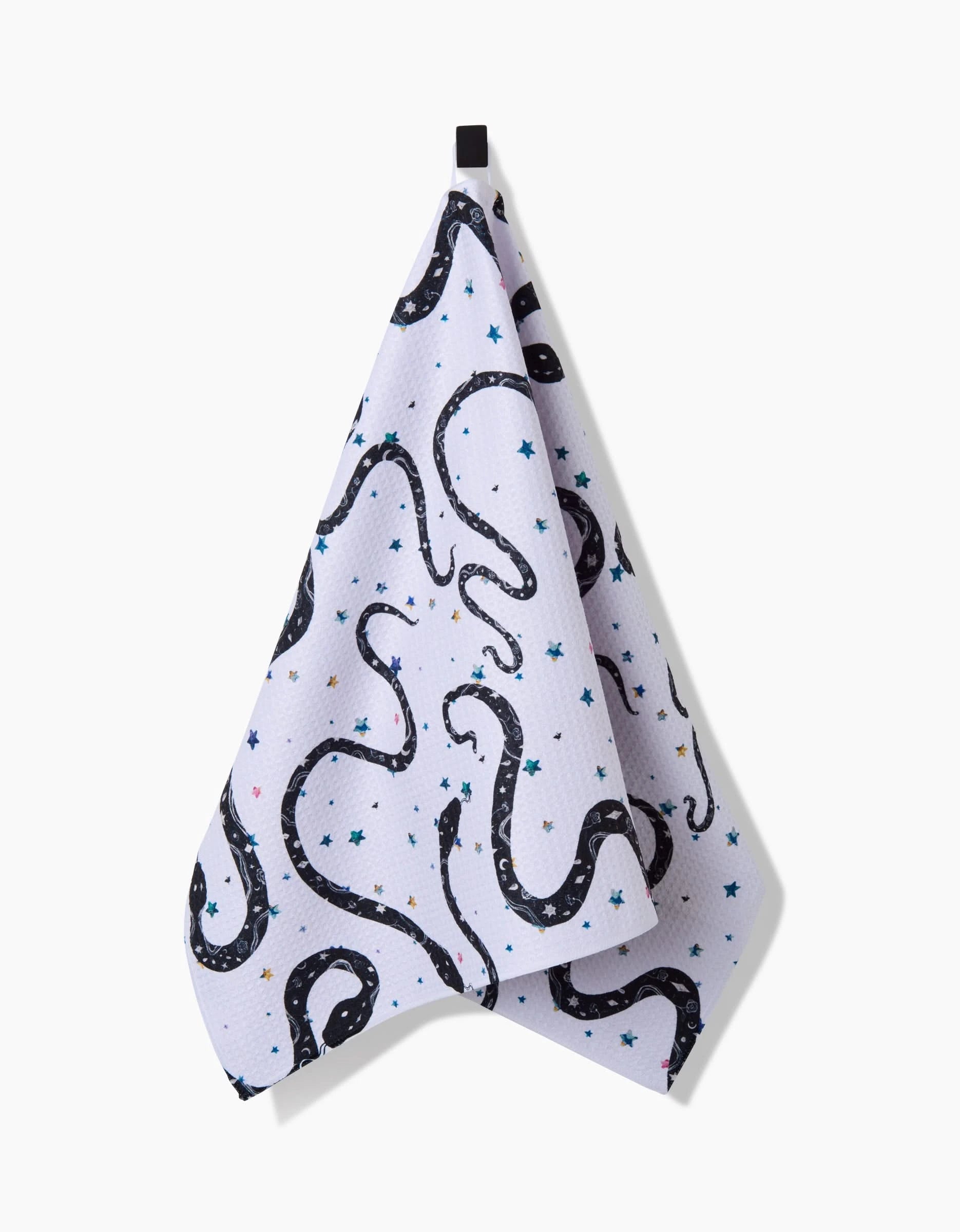 The Cosmic Snakes tea towel by Pascale Dilger, featuring a black snake and blue star pattern, hangs from a black loop against a white background and is crafted from ultra-absorbent recycled materials.