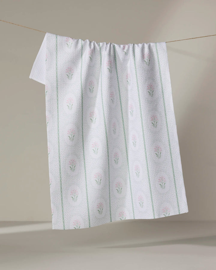 The Hufton Studio Cottage Dainty Spotted recycled kitchen towel, featuring a subtle green pattern and pink floral designs, hangs on a clothesline against a neutral background.