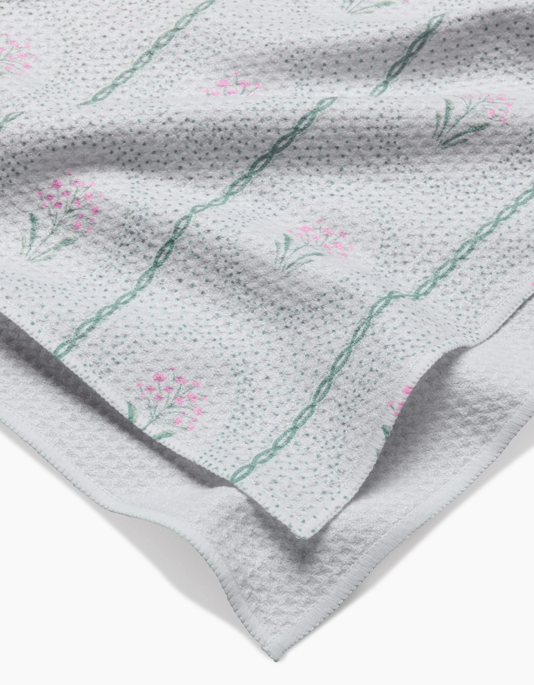 A close-up of the Hufton Studio Cottage Dainty Spotted Kitchen Tea Towel, crafted from ultra-absorbent Geoweave fabric, with green diagonal lines and pink floral clusters, displayed in soft folds.