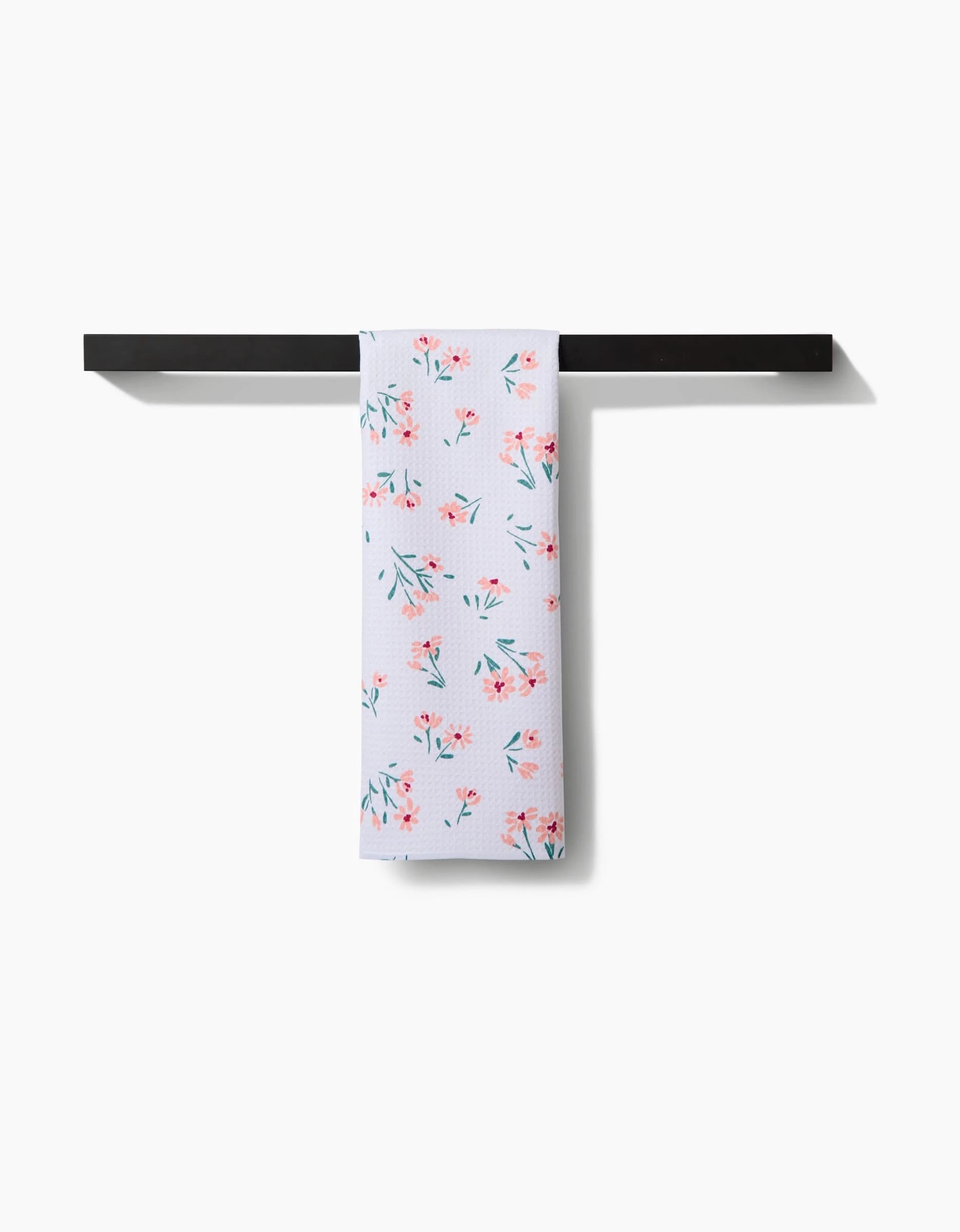 The Cottage Garden tea towel by Hufton Studio, featuring a pink and green floral pattern on Geoweave fabric, hangs neatly folded over a black towel bar against a plain white background.