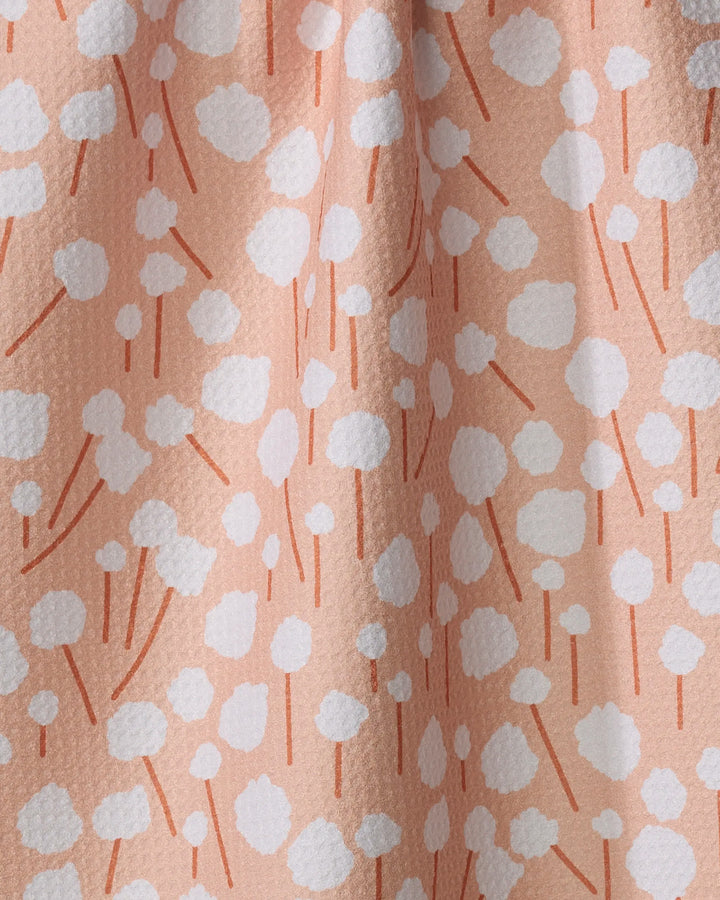 The Cotton Floral tea towel by Coit Creative features a peach hue with scattered white dots and short, thin orange lines, creating a modern floral pattern.