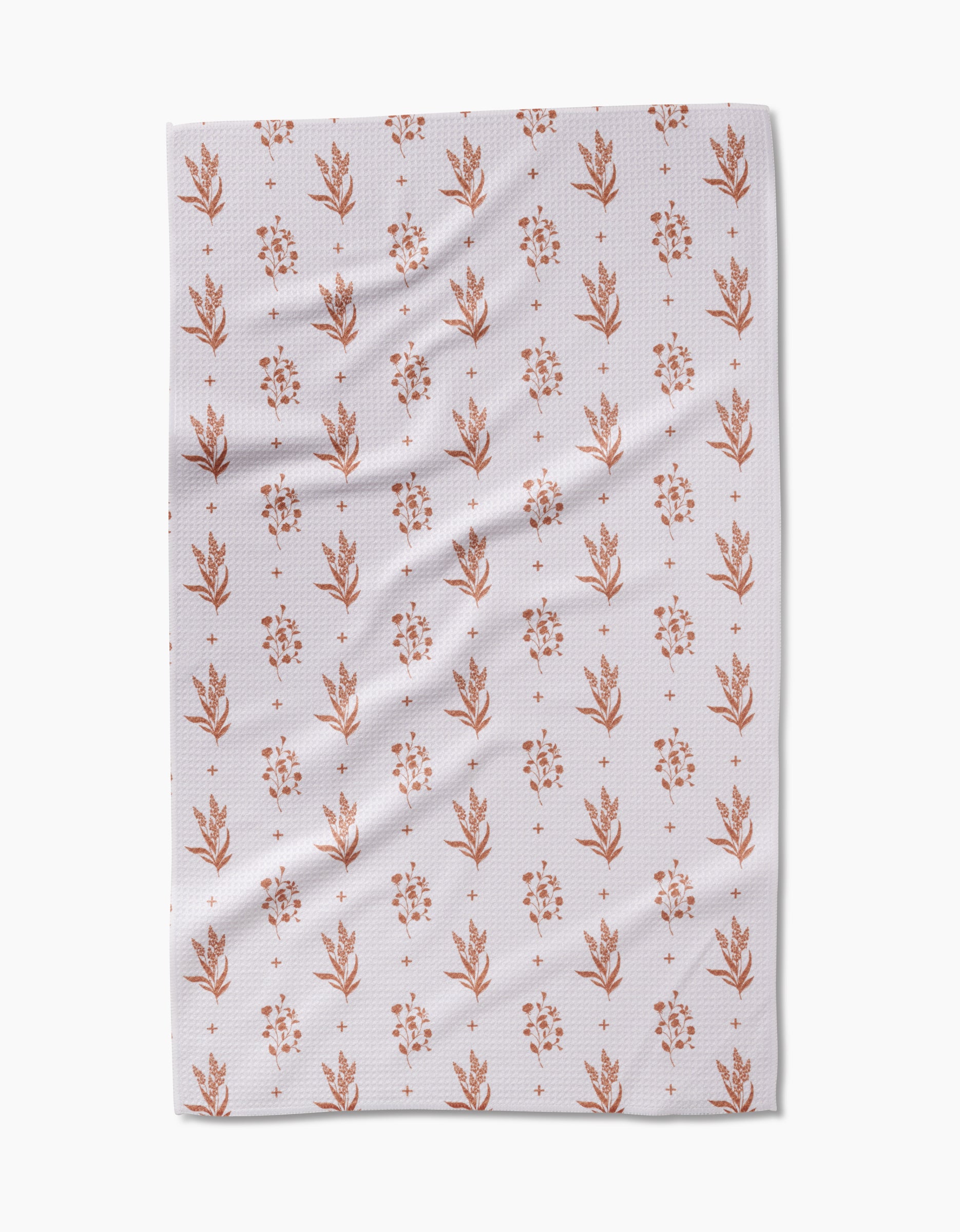 The Country Road tea towel by Charlie Rowan Designs is made from white Geoweave fabric and features a repeating pattern of small, rust floral and leaf motifs arranged in vertical rows. Subtle folds and creases are visible on the fabric.