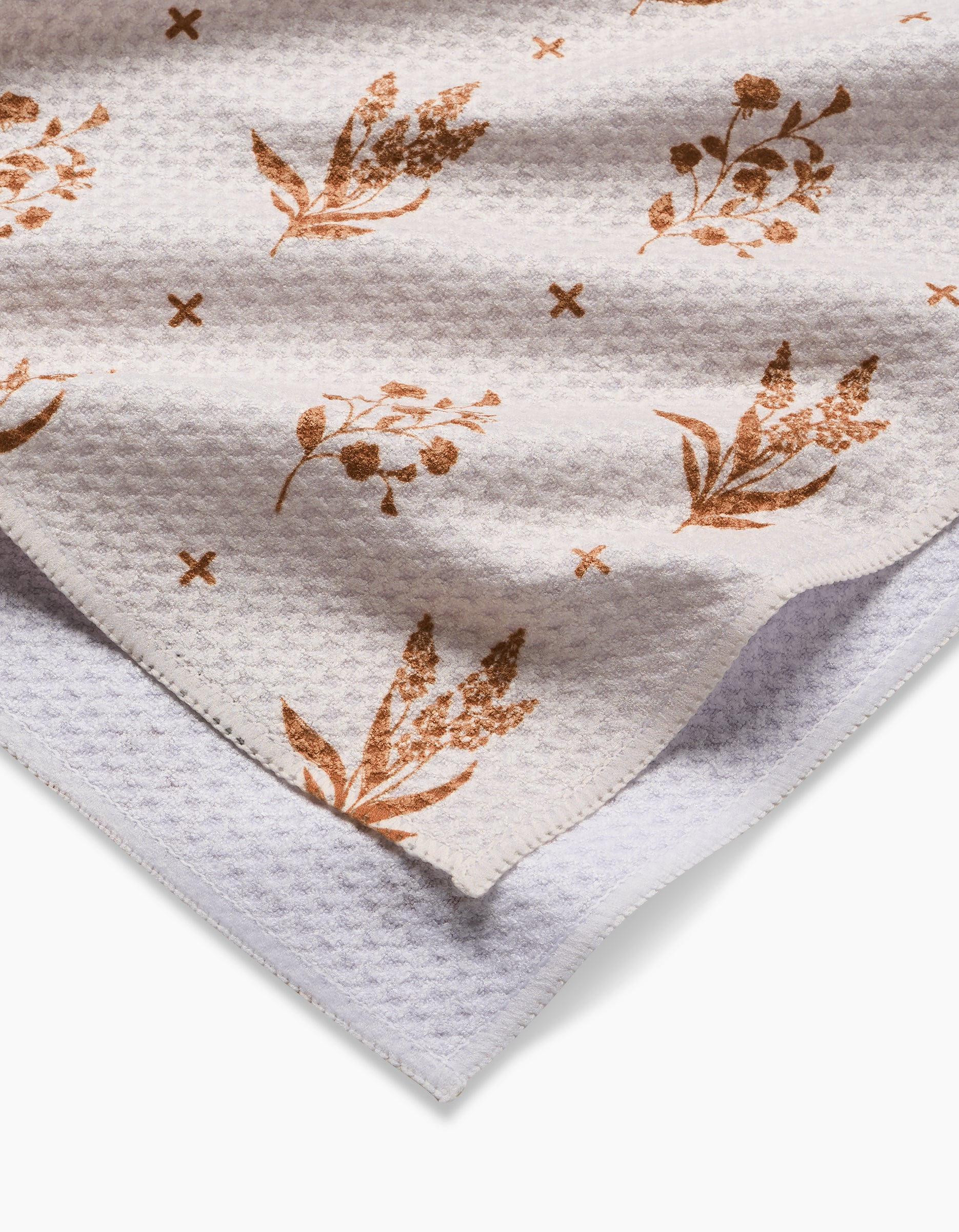 A close-up of the Country Road tea towel by Charlie Rowan Designs shows its white waffle-textured Geoweave fabric, featuring brown floral and cross prints, with one corner folded to display the reverse side.