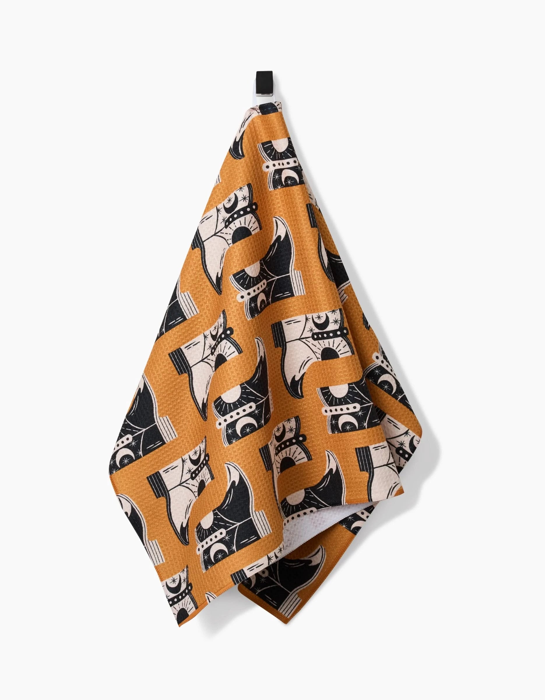 A Megan Roy Cowboy Boots Tea Towel, featuring a playful boot pattern, made from ultra-absorbent Geoweave fabric, hangs from a black loop against a white wall.