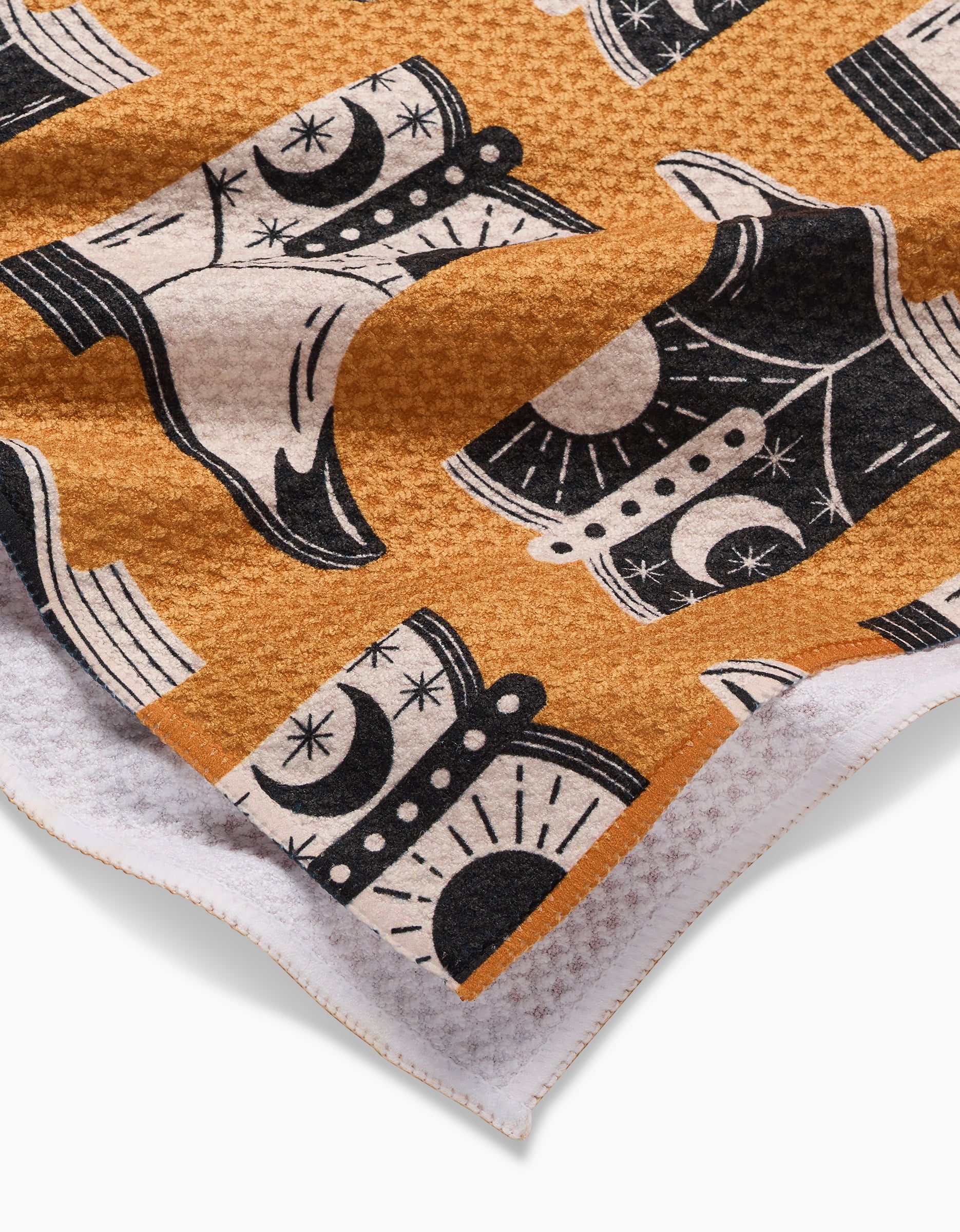 Close-up of Megan Roys Cowboy Boots Geoweave tea towel, ultra-absorbent with waffle texture, featuring black and white cowboy boots with moons and stars on mustard yellow and a white edge.