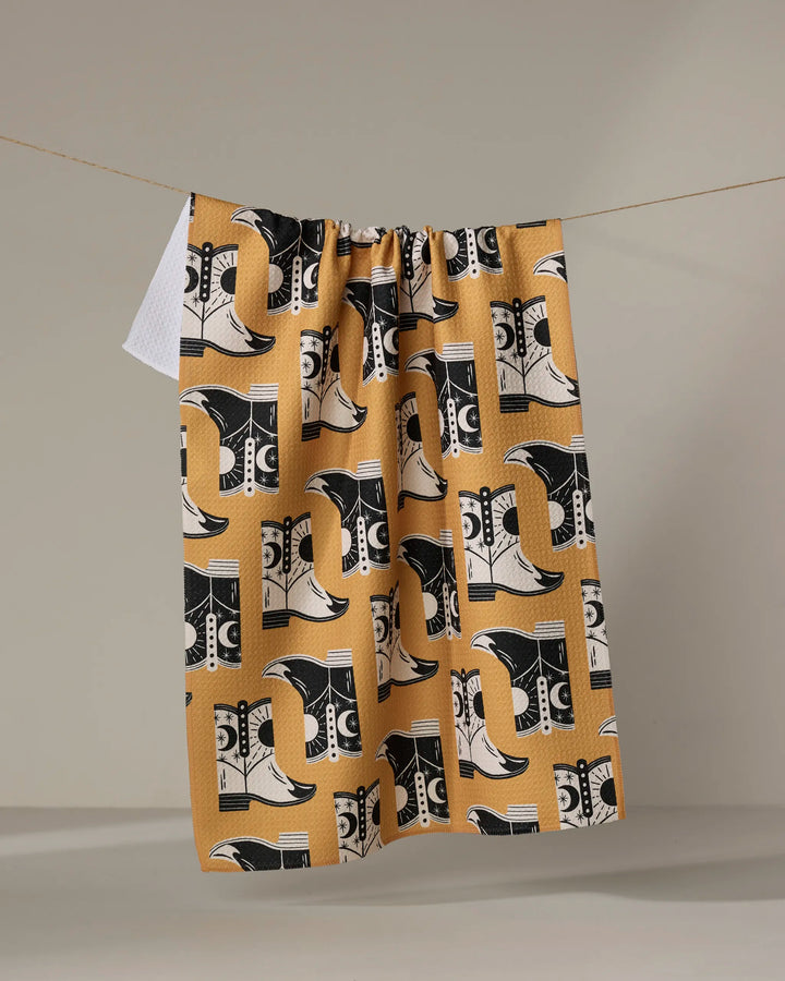 Cowboy Boots by Megan Roy, crafted from quality materials in a mustard yellow hue with bold black and white abstract details, rest with soft shadows and gentle curves against a neutral background.