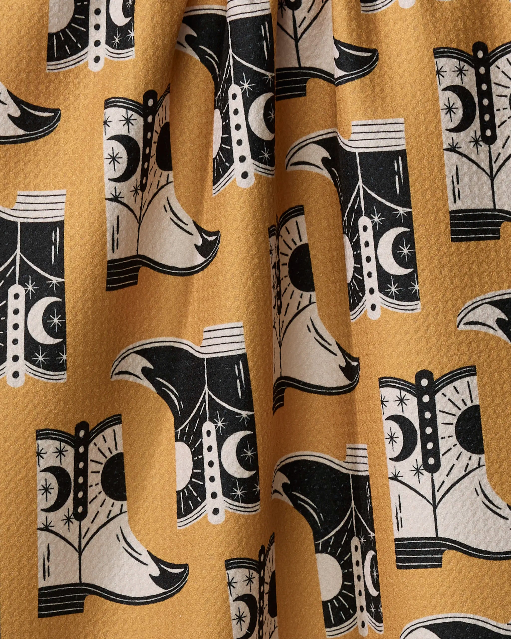 A close-up of Megan Roy’s "Cowboy Boots" quick-drying yellow fabric, featuring a repeating black and white cowboy boot pattern with moon and star motifs. The material is slightly wrinkled.