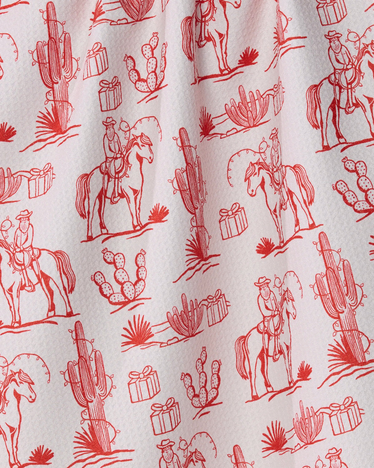 Geometry’s “Cowboy Claus” tea towel features playful red line illustrations of cowboys on horses, cacti, wrapped gifts, and desert plants repeating across a textured white fabric for a delightful western holiday motif. Ultra-absorbent and stylish, this kitchen towel is perfect for drying dishes or adding festive flair to your home décor.