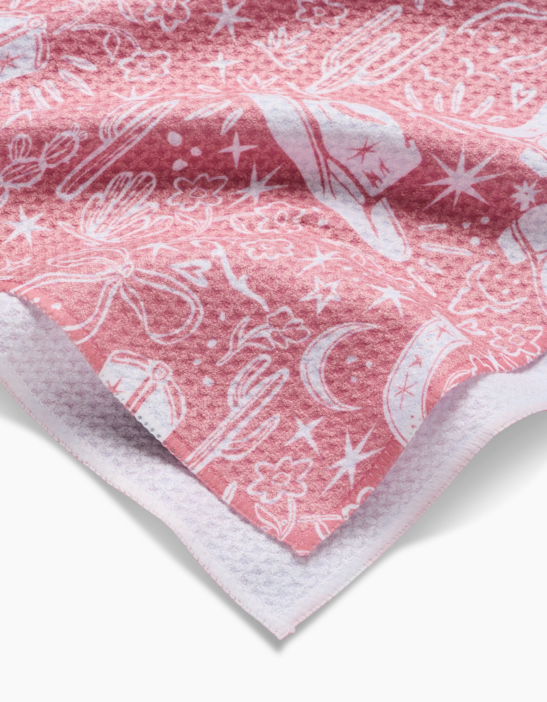 A close-up of the Cowgirl Chic pink towel, adorned with white cowboy hats, cacti, boots, stars, moons, and flowers. Crafted from ultra-absorbent Geoweave fabric, it features a textured edge and a soft waffle-like pattern.