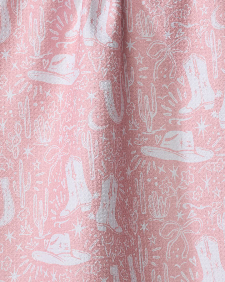 Add a touch of flair to your kitchen with the Cowgirl Chic dish towel by Aubrey Fairchild. This pink, absorbent towel features a white western motif with cowboy hats, boots, cacti, stars, and lassos in softly gathered folds.