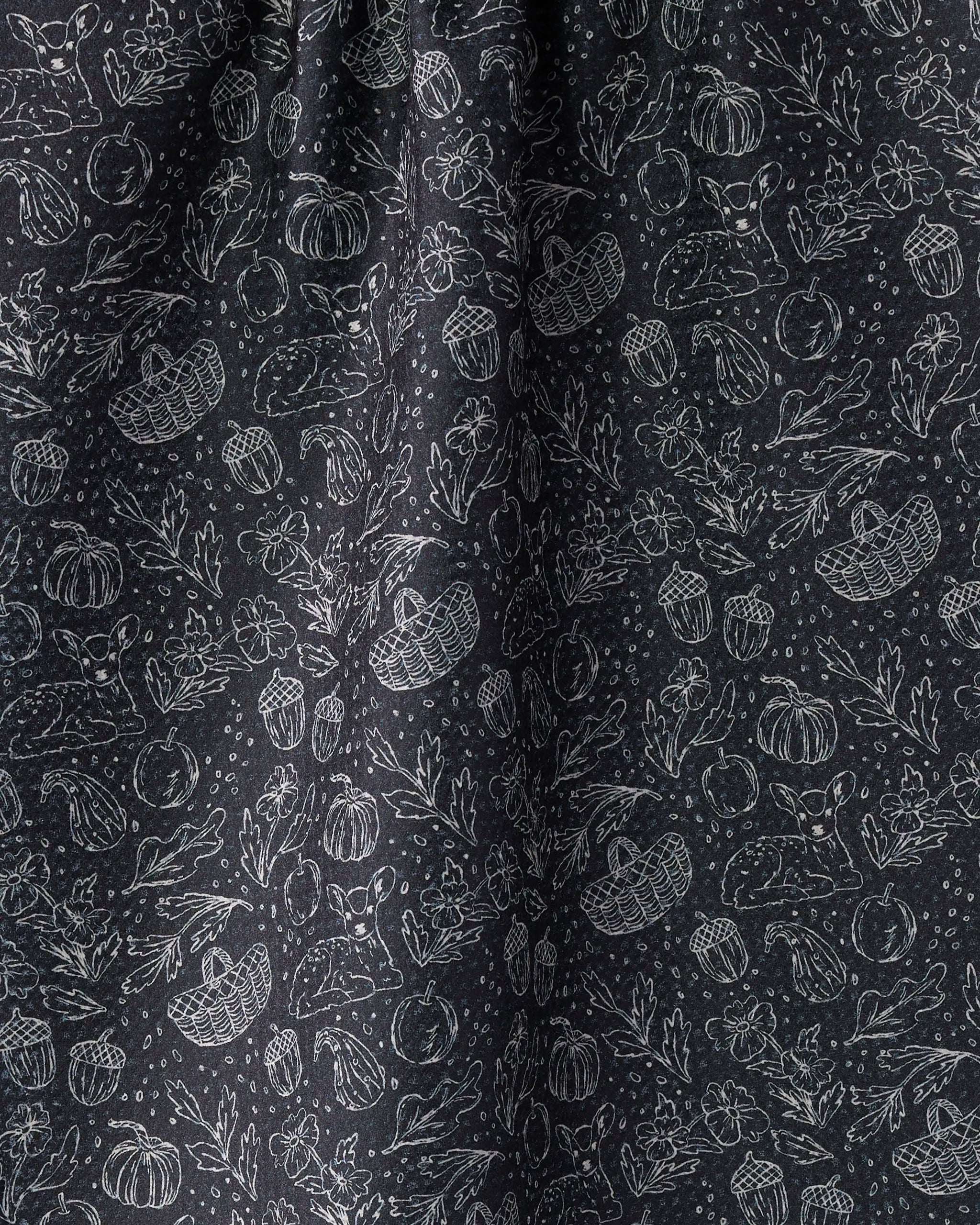 The Geometry Cozy Flora is a black kitchen tea towel with a white, hand-drawn fall pattern—pumpkins, acorns, baskets, leaves, flowers, and mushrooms. Ultra-absorbent and detailed, it’s made from recycled materials.