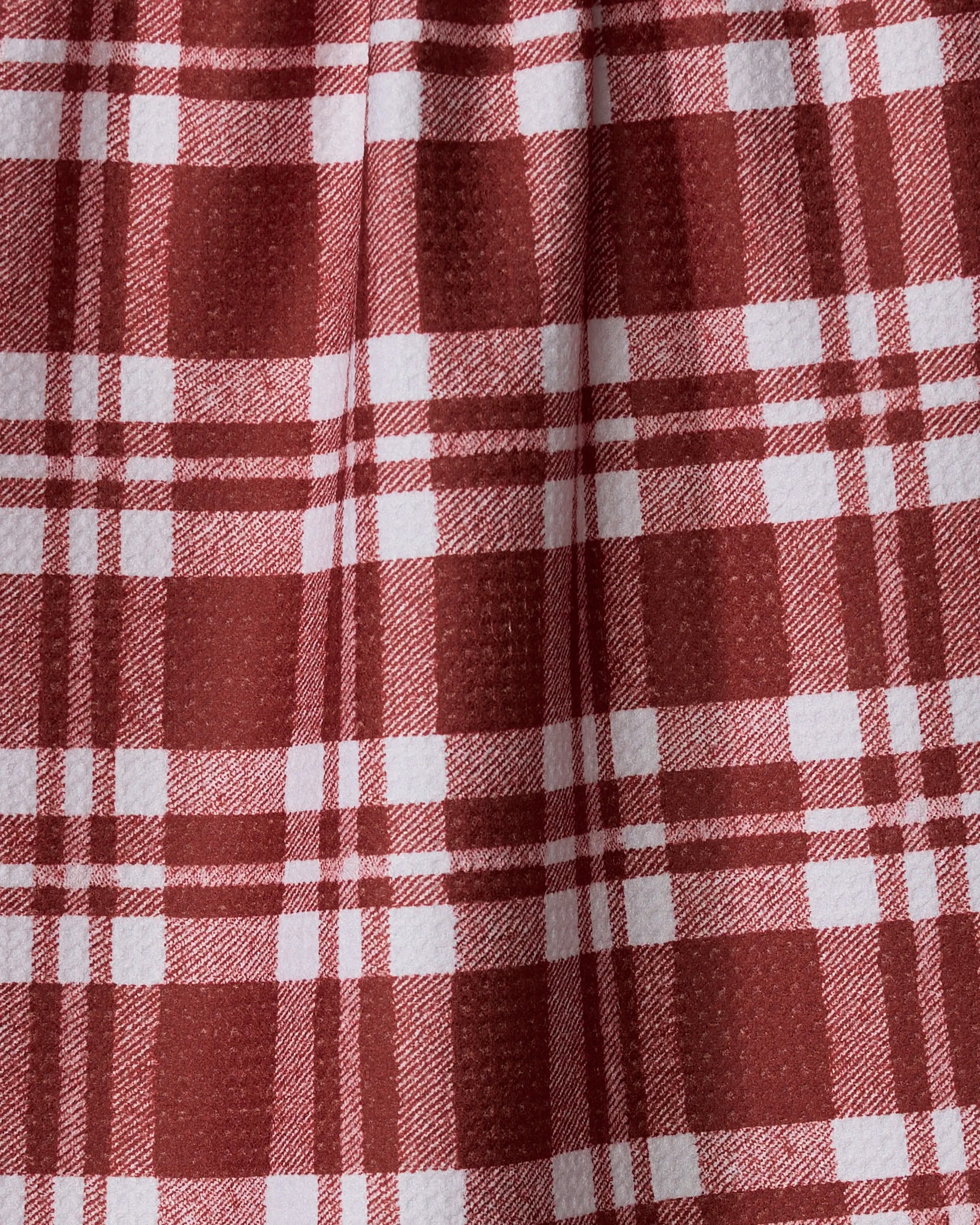 Close-up of the Cranleigh dish towel by Geometry, featuring a red and white plaid woven texture with intersecting checkered lines. Gentle folds add shadows and depth to this absorbent, practical kitchen textile.