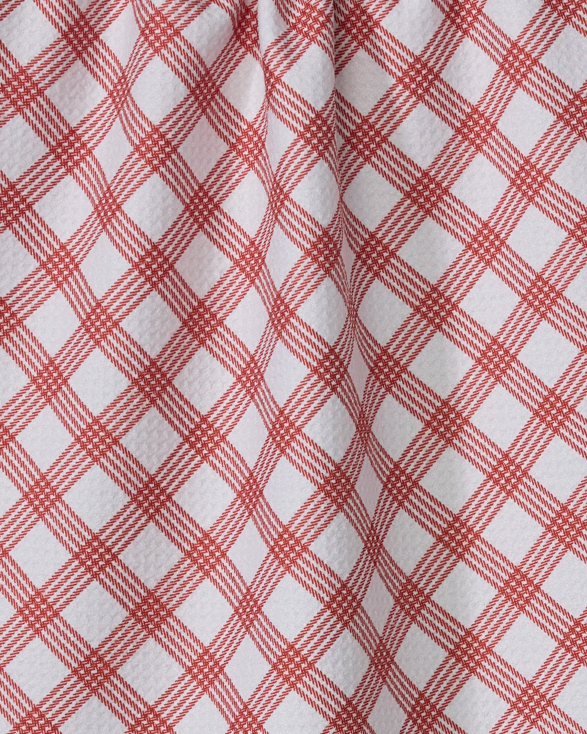 The Crimson Wrap by Geometry features white fabric with a red crisscross plaid pattern, forming a diamond-shaped grid. Its gentle folds add subtle shadows and texture, evoking the look of a classic tea towel.