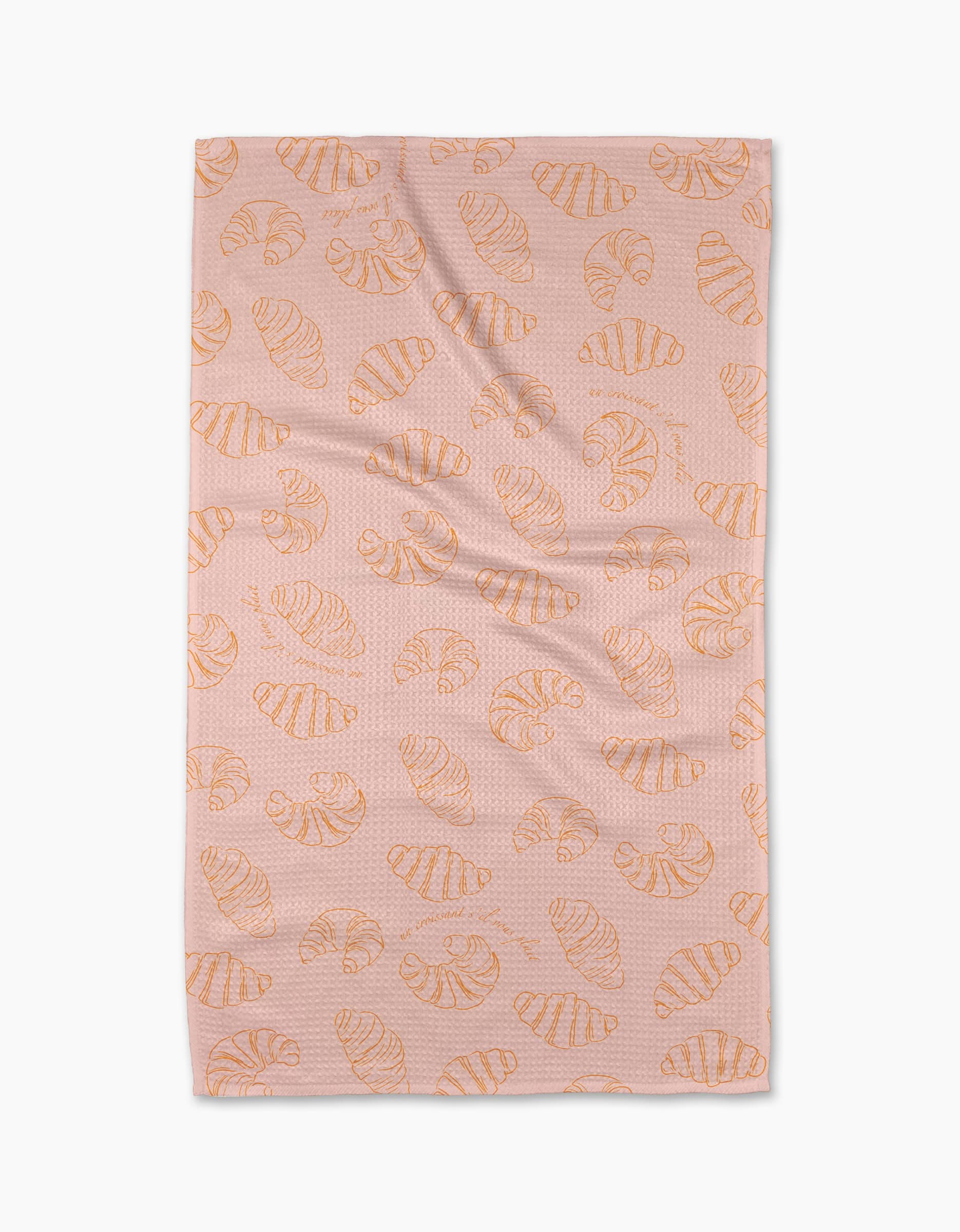 The Croissant Crush tea towel by Geometry, made from recycled materials, features orange croissants on pink and is shown laid flat against a white background.