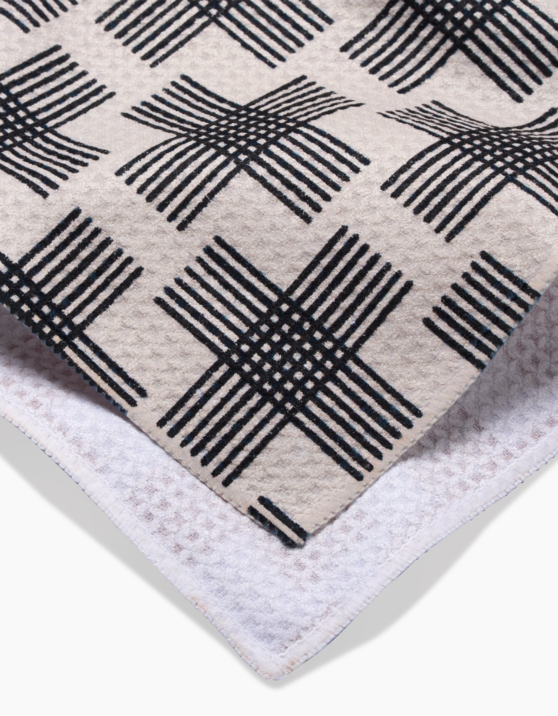 A close-up of the Cross Hatch Geoweave Tea Towel by Rosa Kichline, showcasing a black and beige geometric grid on one side and a white textured reverse.