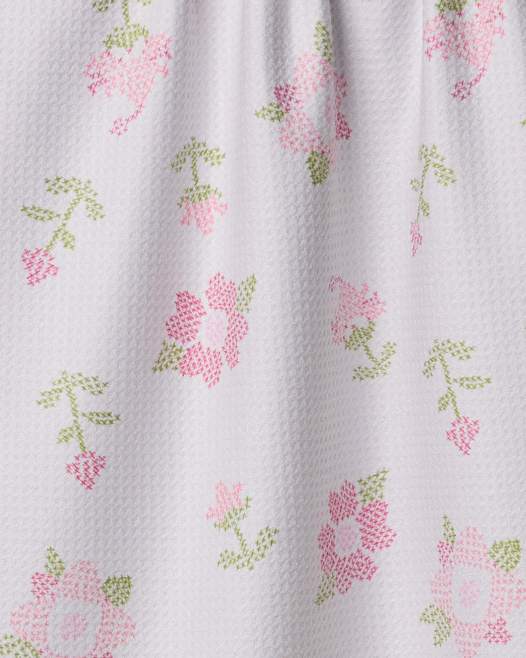 Close-up of Geometry's Cross Stitch Floral tea towel, featuring a white textured fabric with a pink and green cross-stitched flower and leaf pattern that adds charming, delicate detail to your kitchen décor.