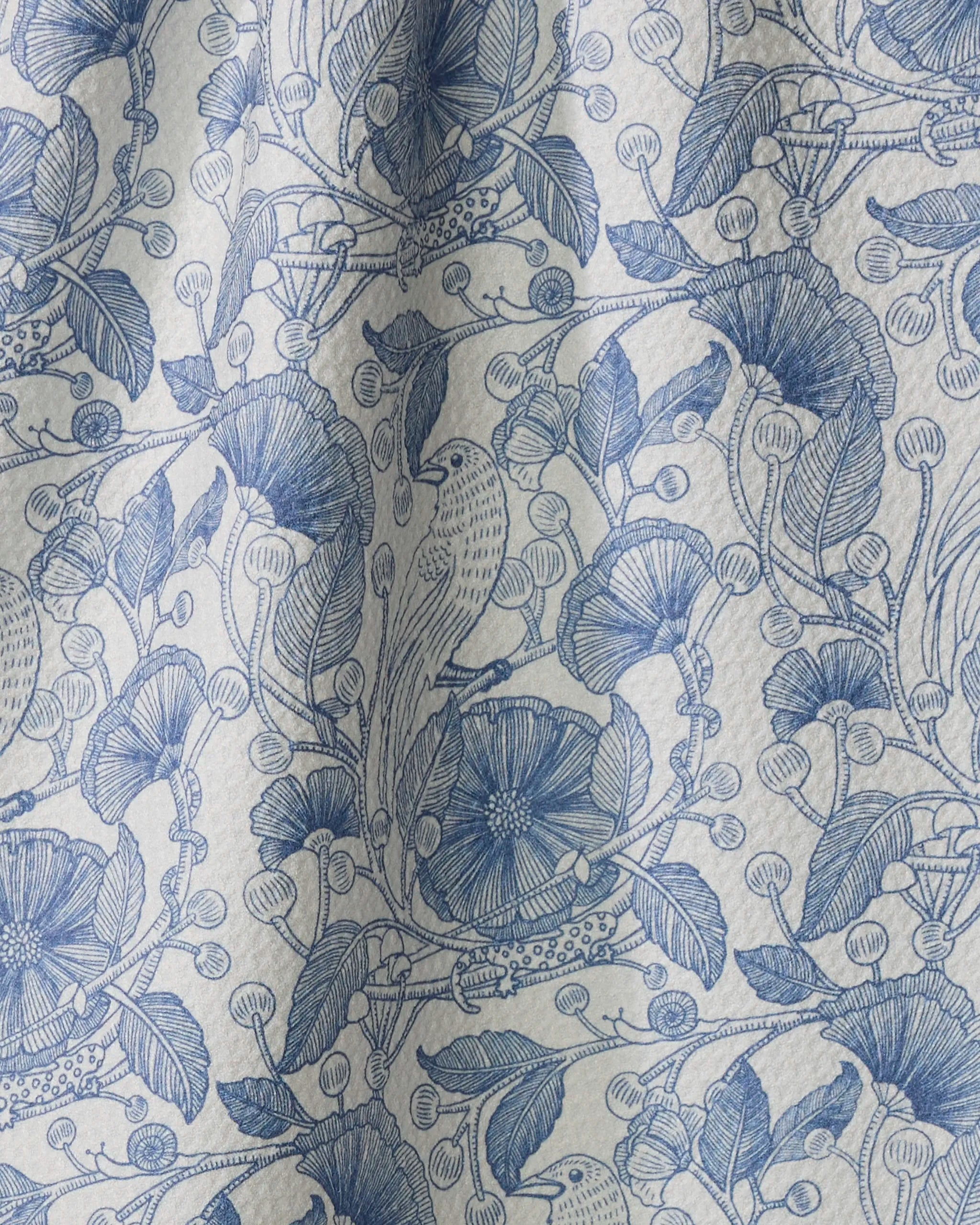 The Katie O'Shea "Crowberries" tea towel features blue and white hand-drawn botanical patterns with flowers, leaves, berries, and birds on gently pleated fabric—adding charm and texture to any kitchen.